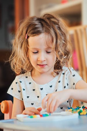 Child playing with colorful pegs on a white board
