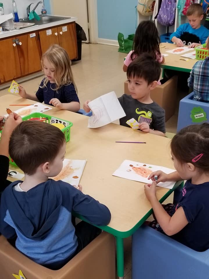 Children sitting at tables in a classroom, drawing and looking at papers