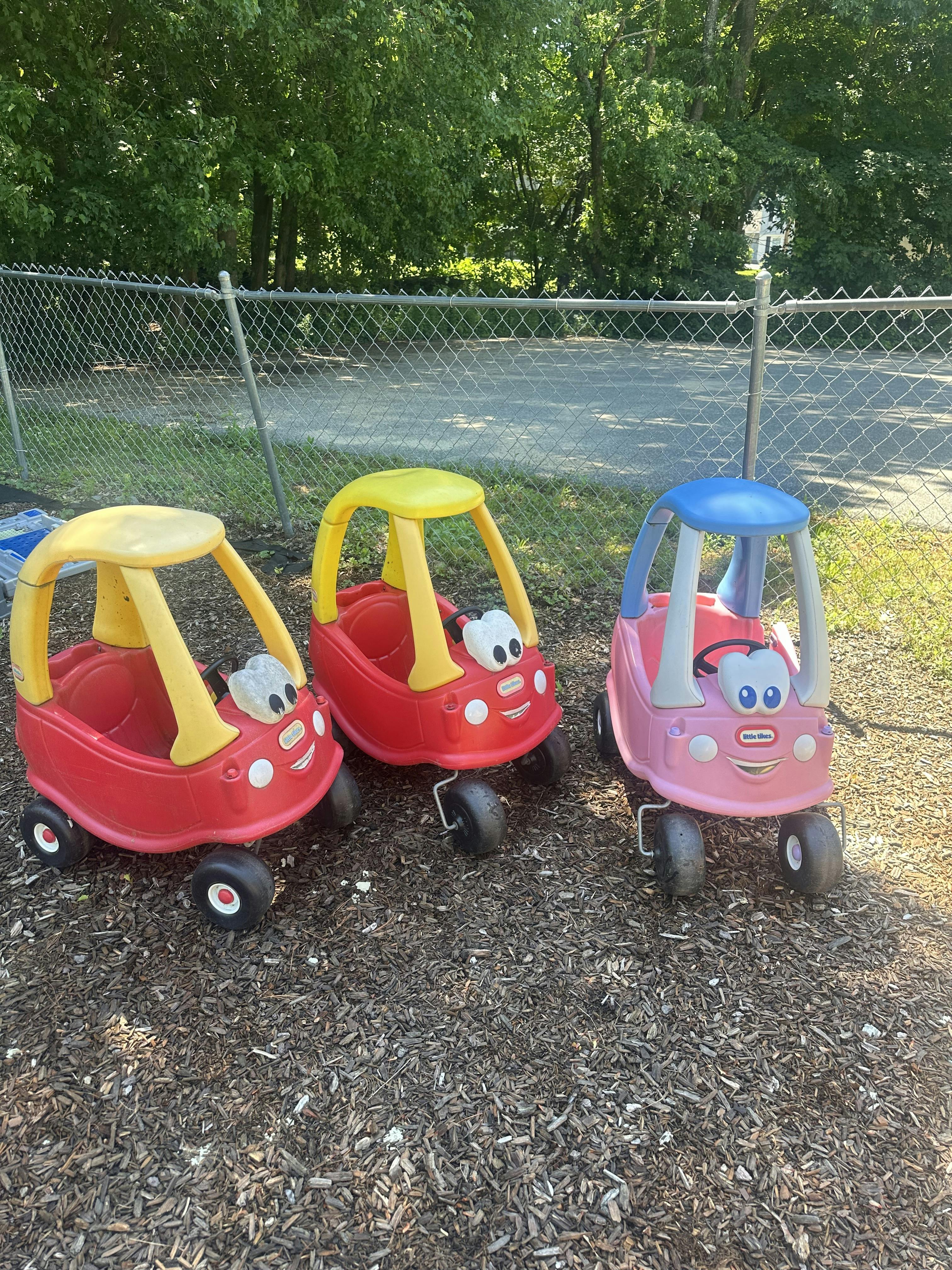 Three toy cars on mulch near a chain-link fence