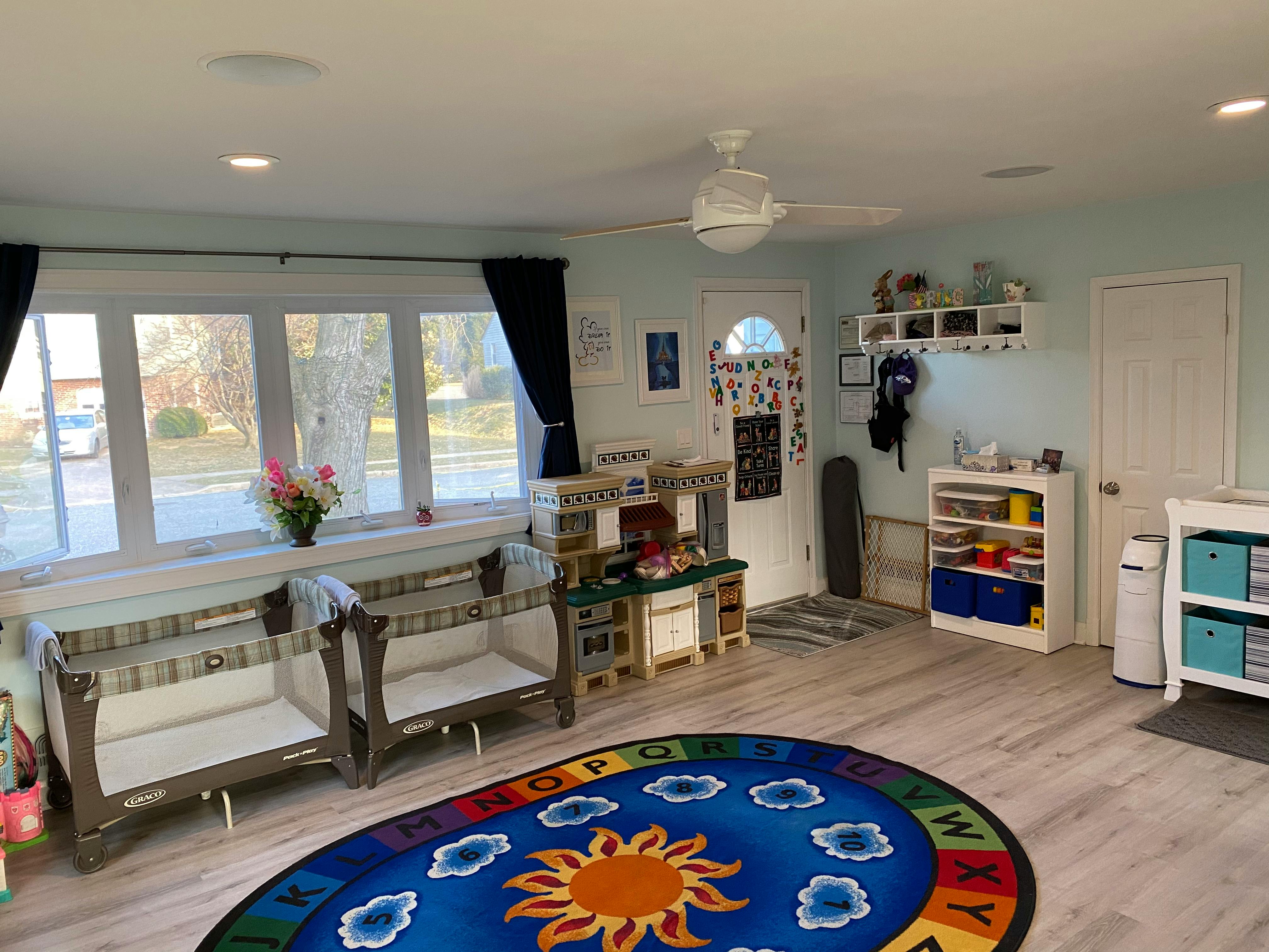 Playroom with two cribs, a play kitchen, and a sun-themed rug
