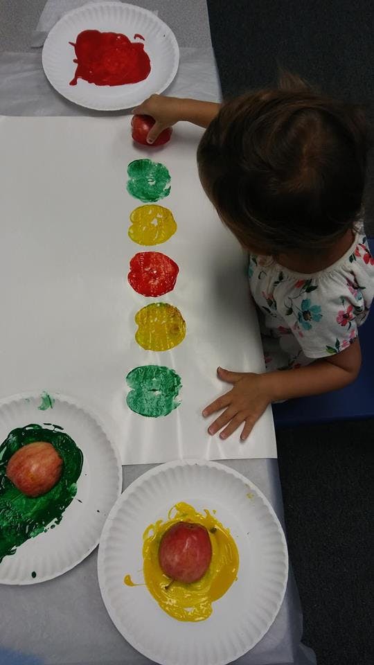 Child making apple prints with red, green, and yellow paint