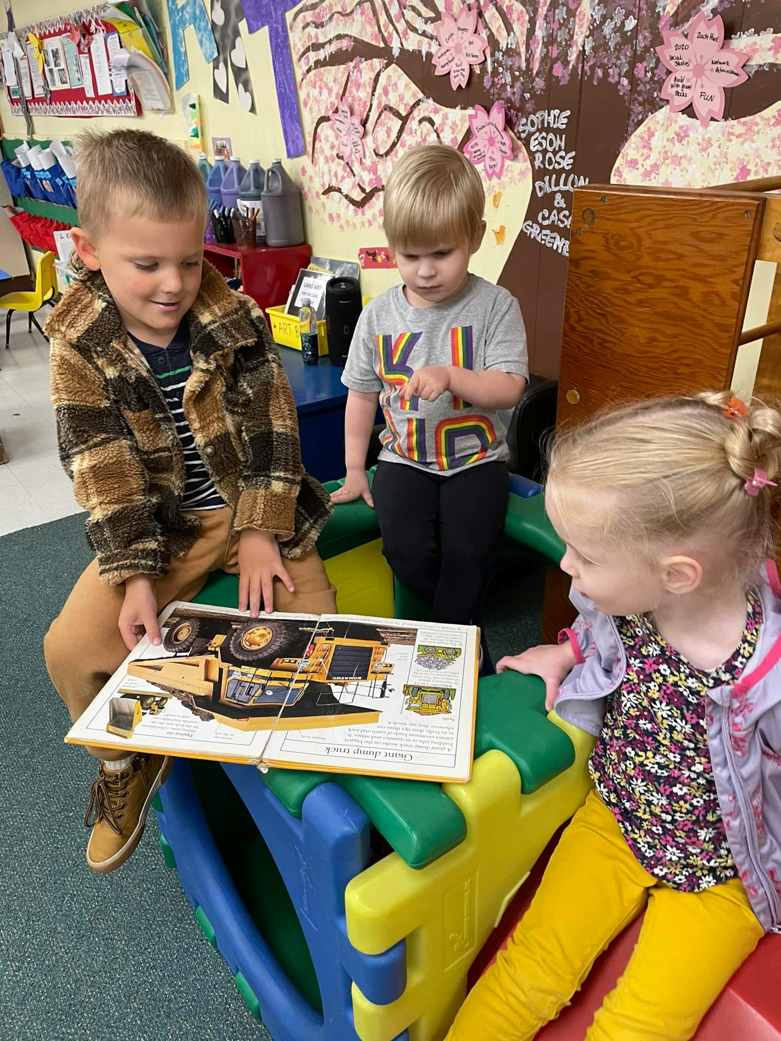 Three children looking at a book with a construction vehicle