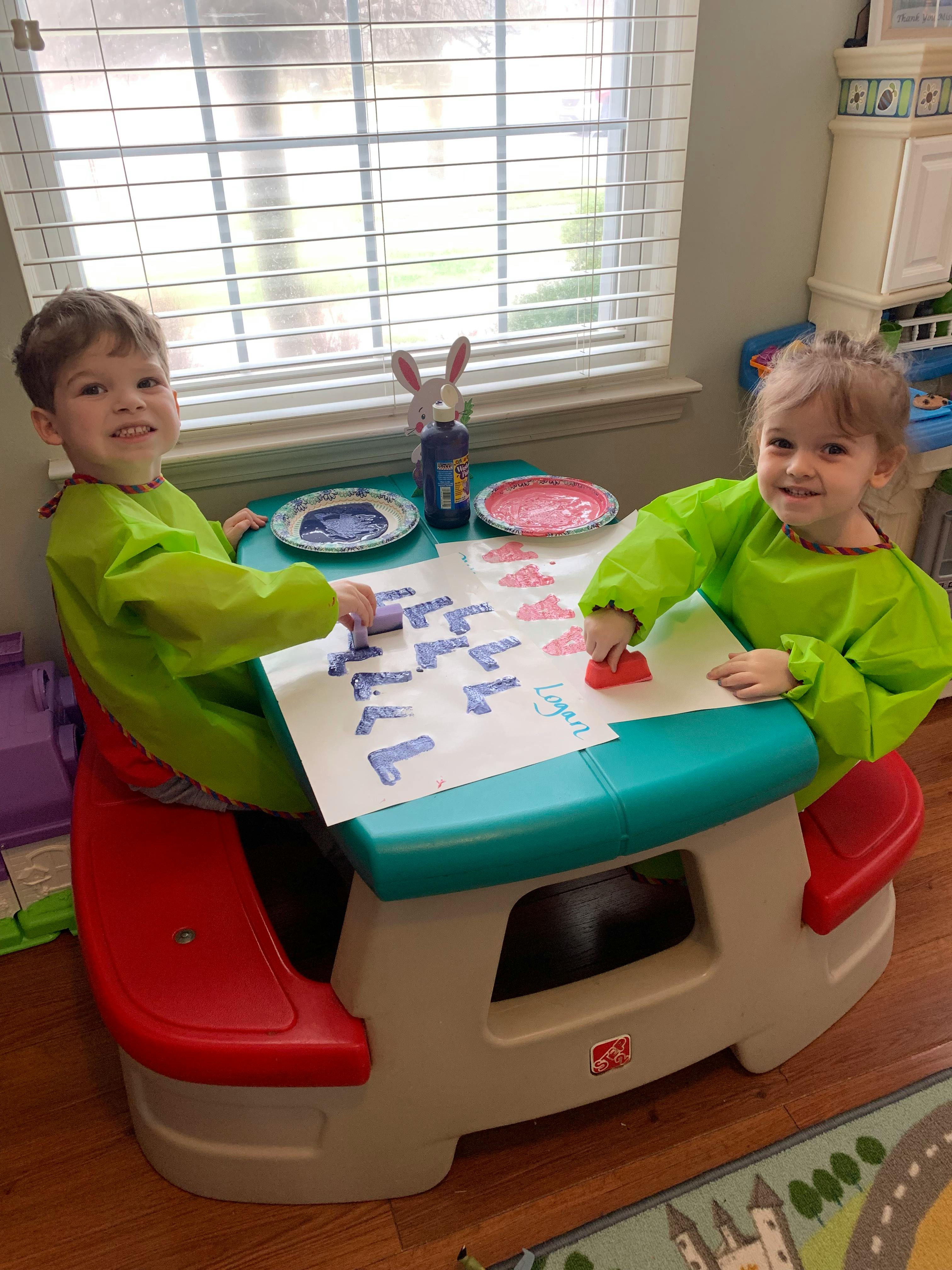 Two children in smocks painting at a small table