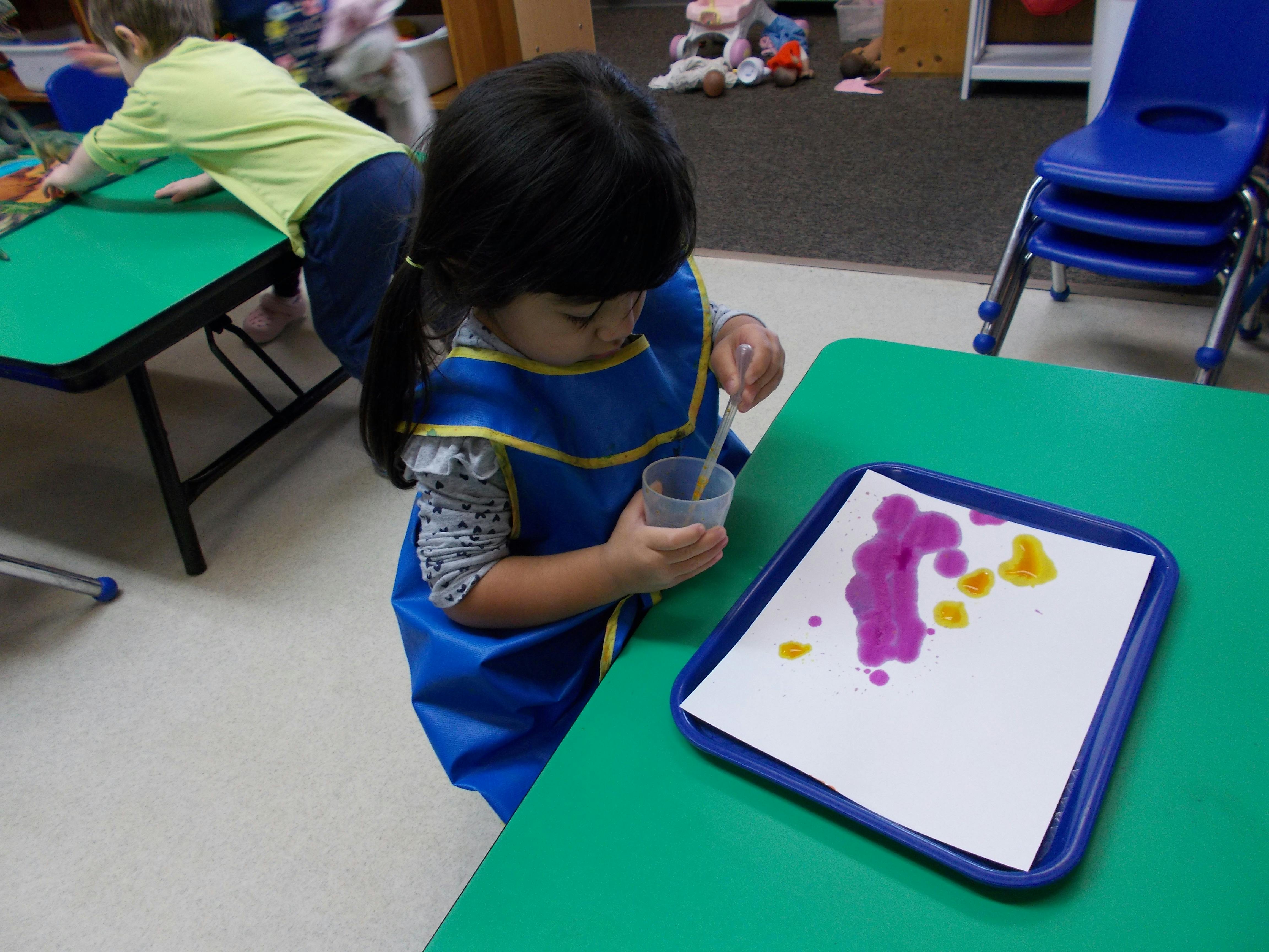 Child in an apron painting with a dropper at a table