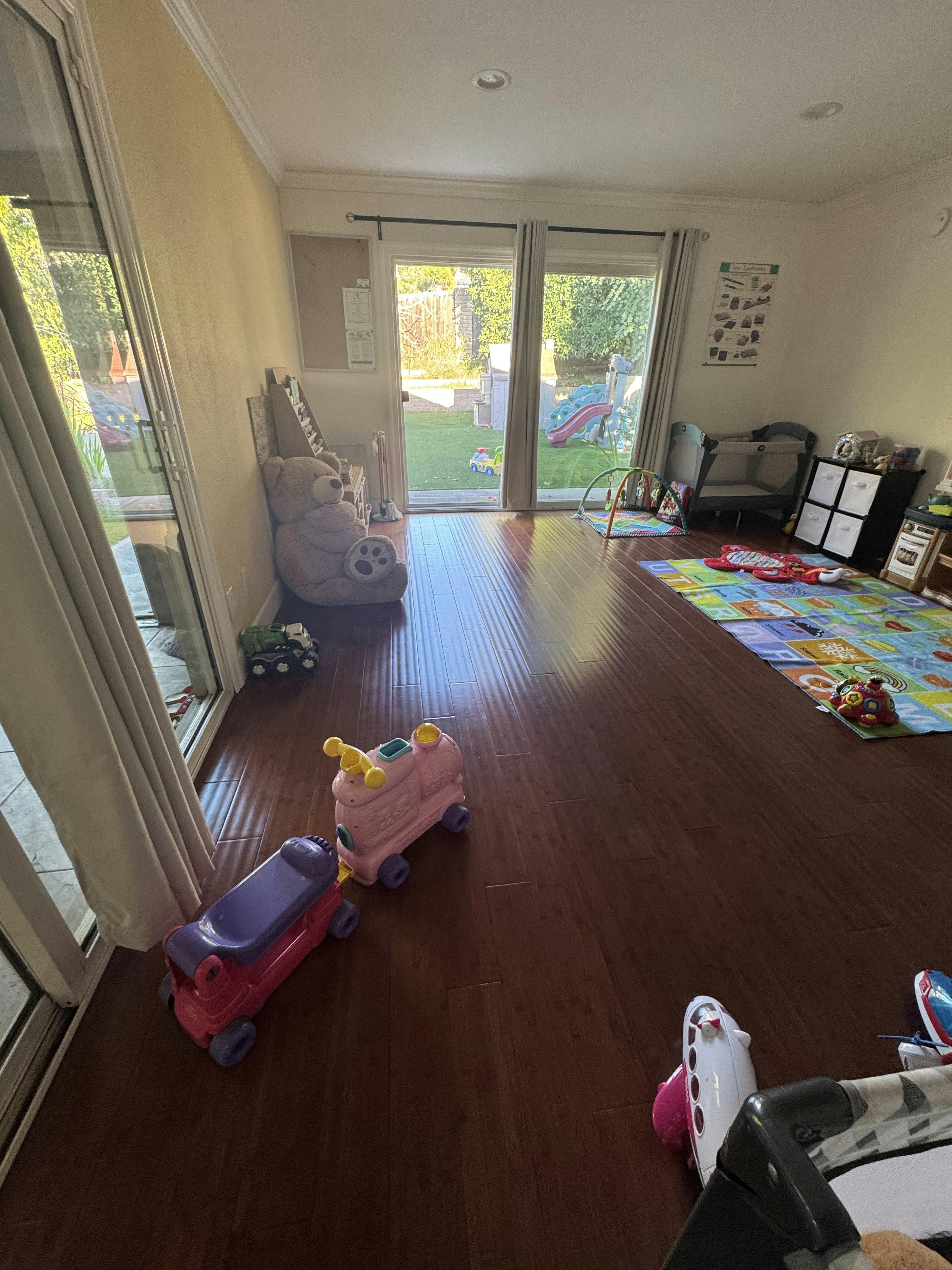 Playroom with toys on a wooden floor and glass doors leading to a backyard