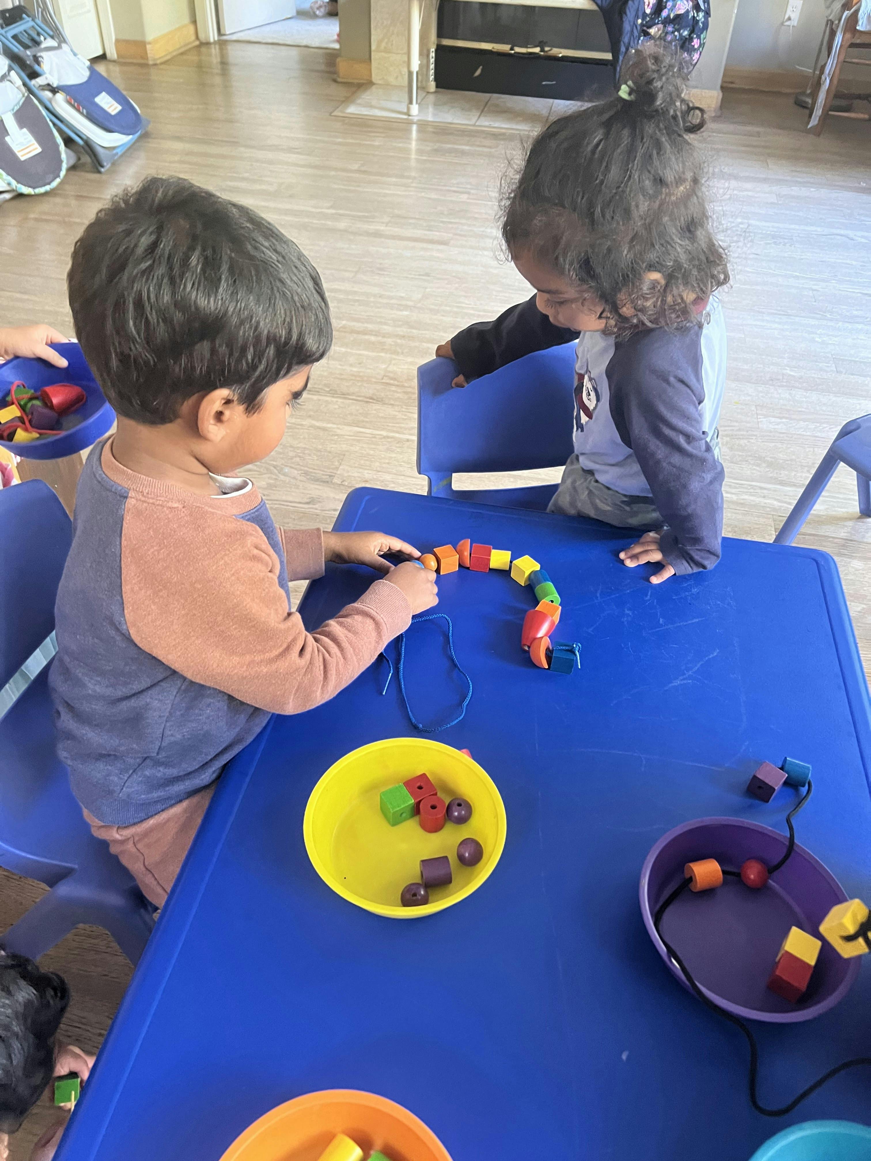 Two children stringing colorful beads at a blue table