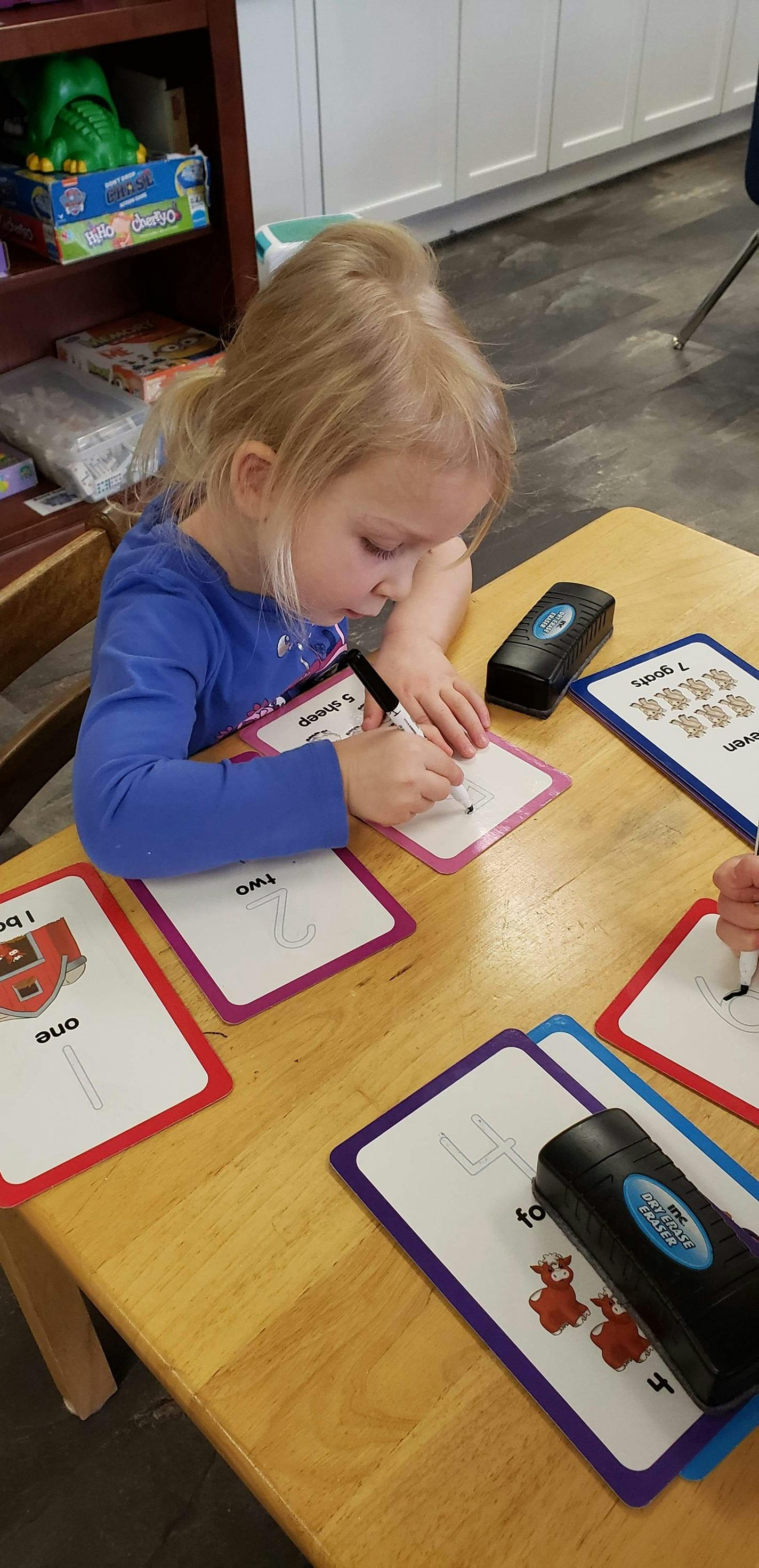 Child writing on a learning card at a table