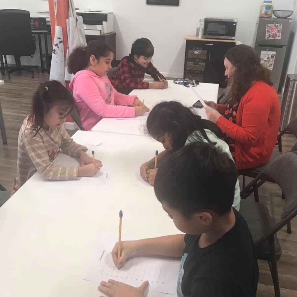 Adult and children writing at a table in a classroom