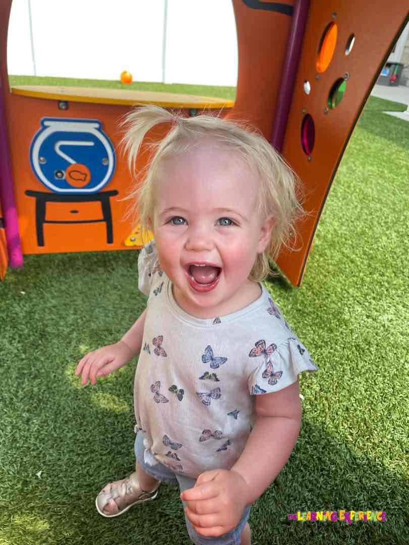 Child with blonde hair and open mouth standing on artificial grass