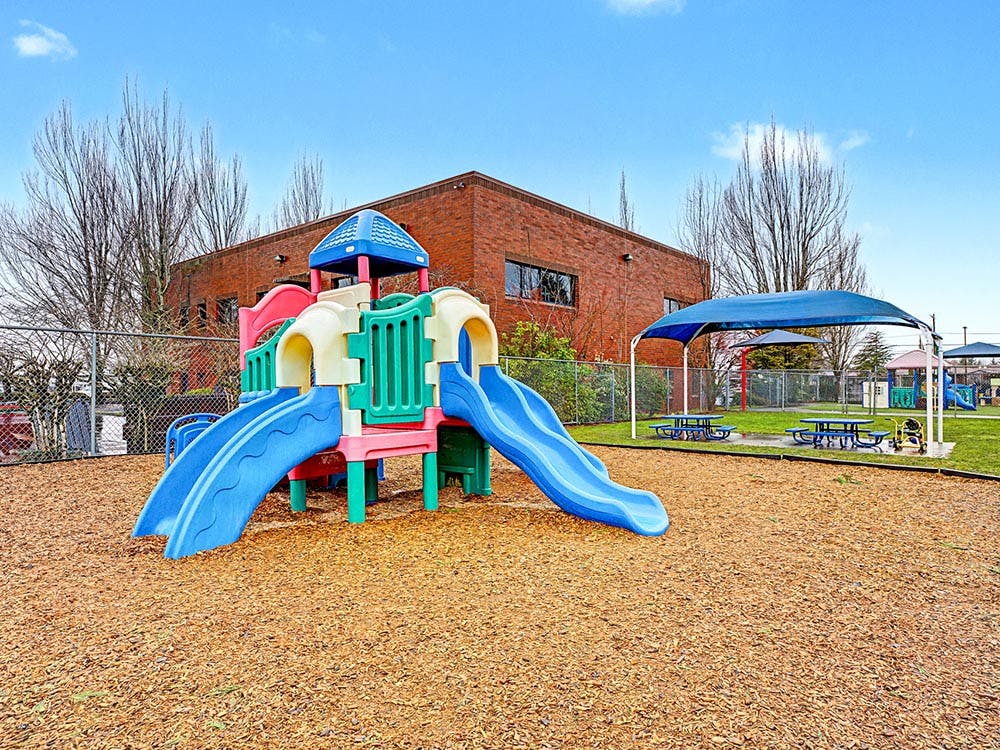 Colorful playground structure with slides on wood chips next to a brick building