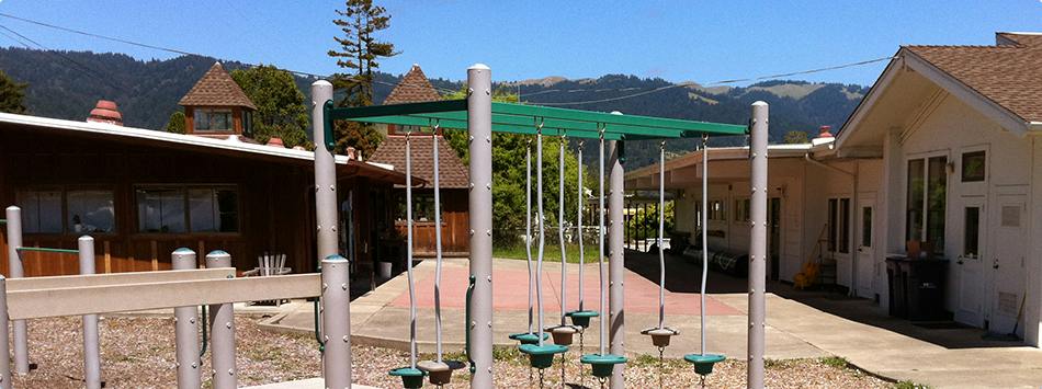 Playground structure with a green canopy and buildings in the background