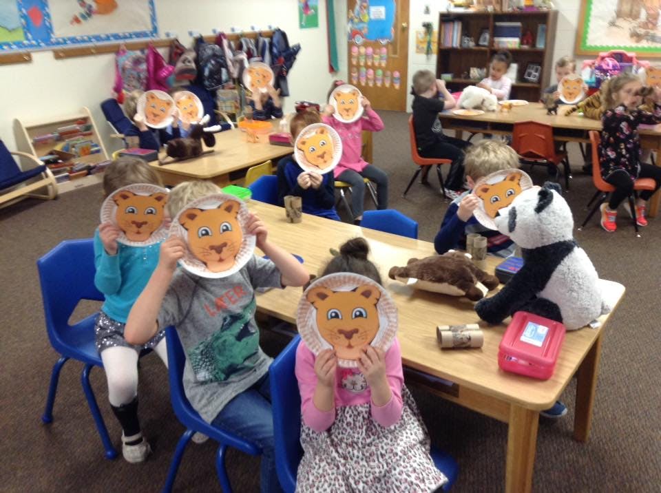 Children holding up paper plate lion masks in a classroom