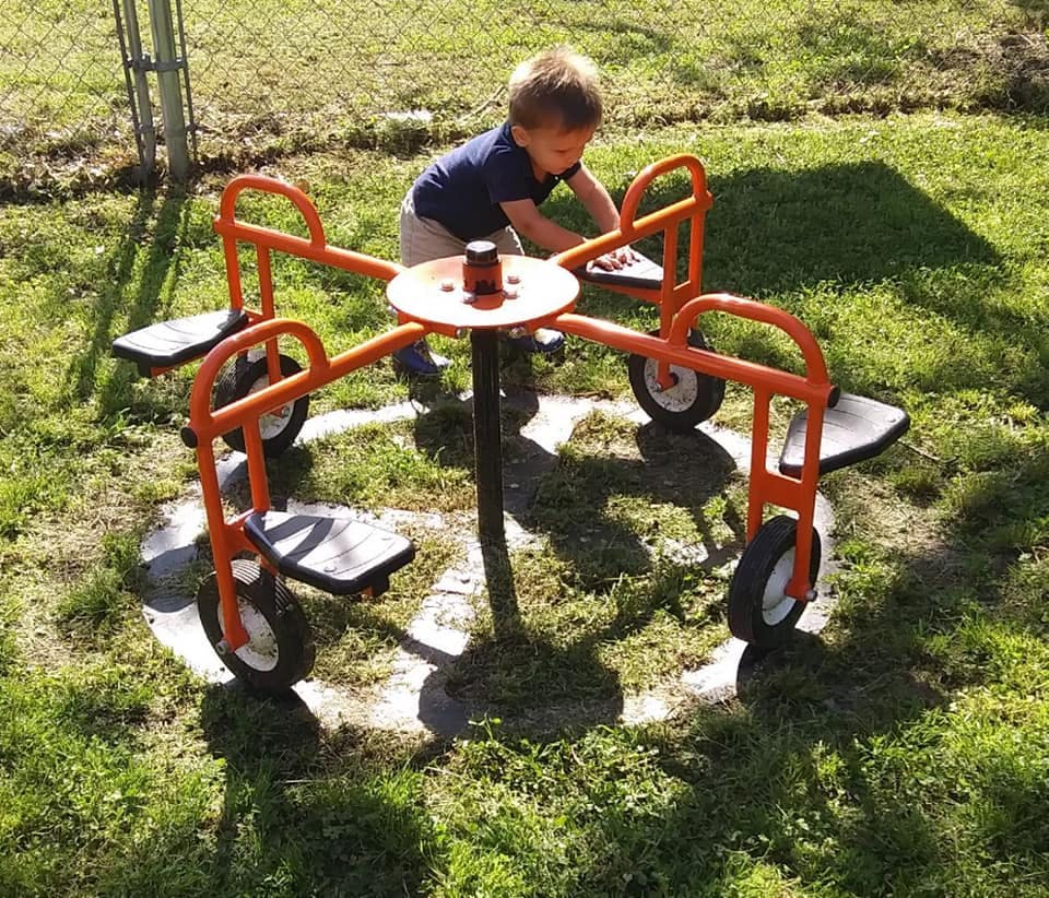 Child playing on a merry-go-round in a grassy area
