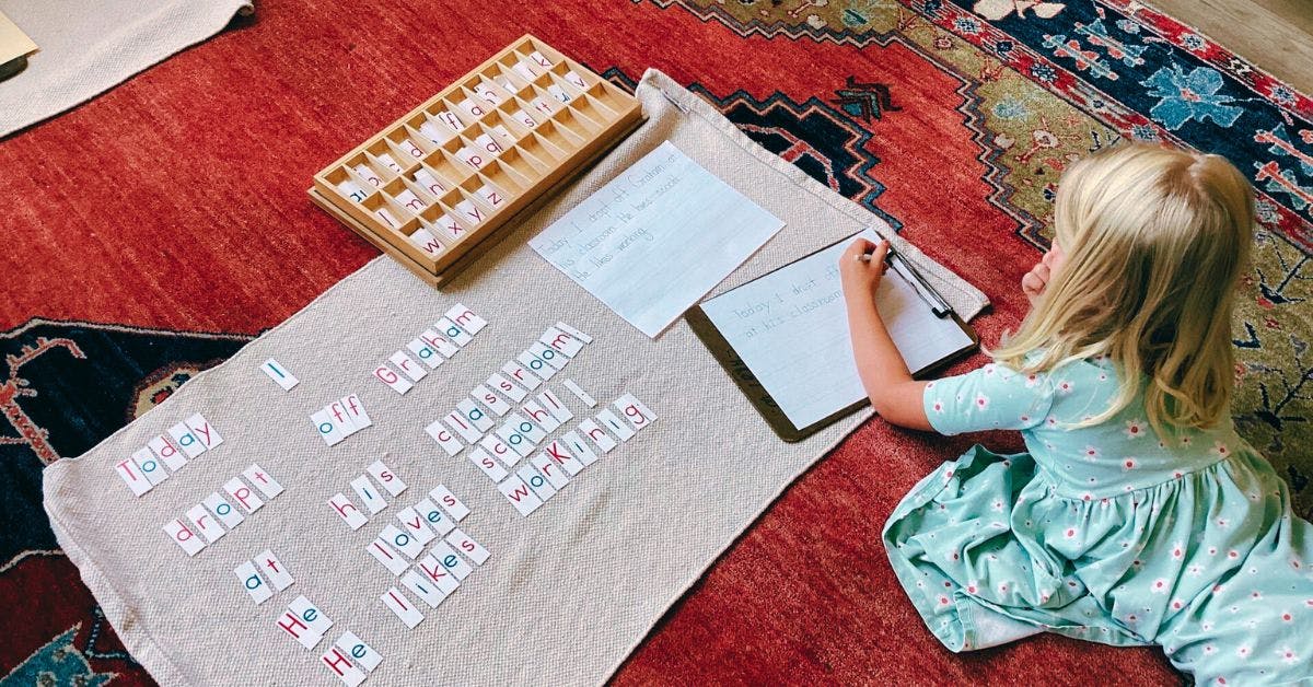 Child writing on paper next to a wooden box and number cards
