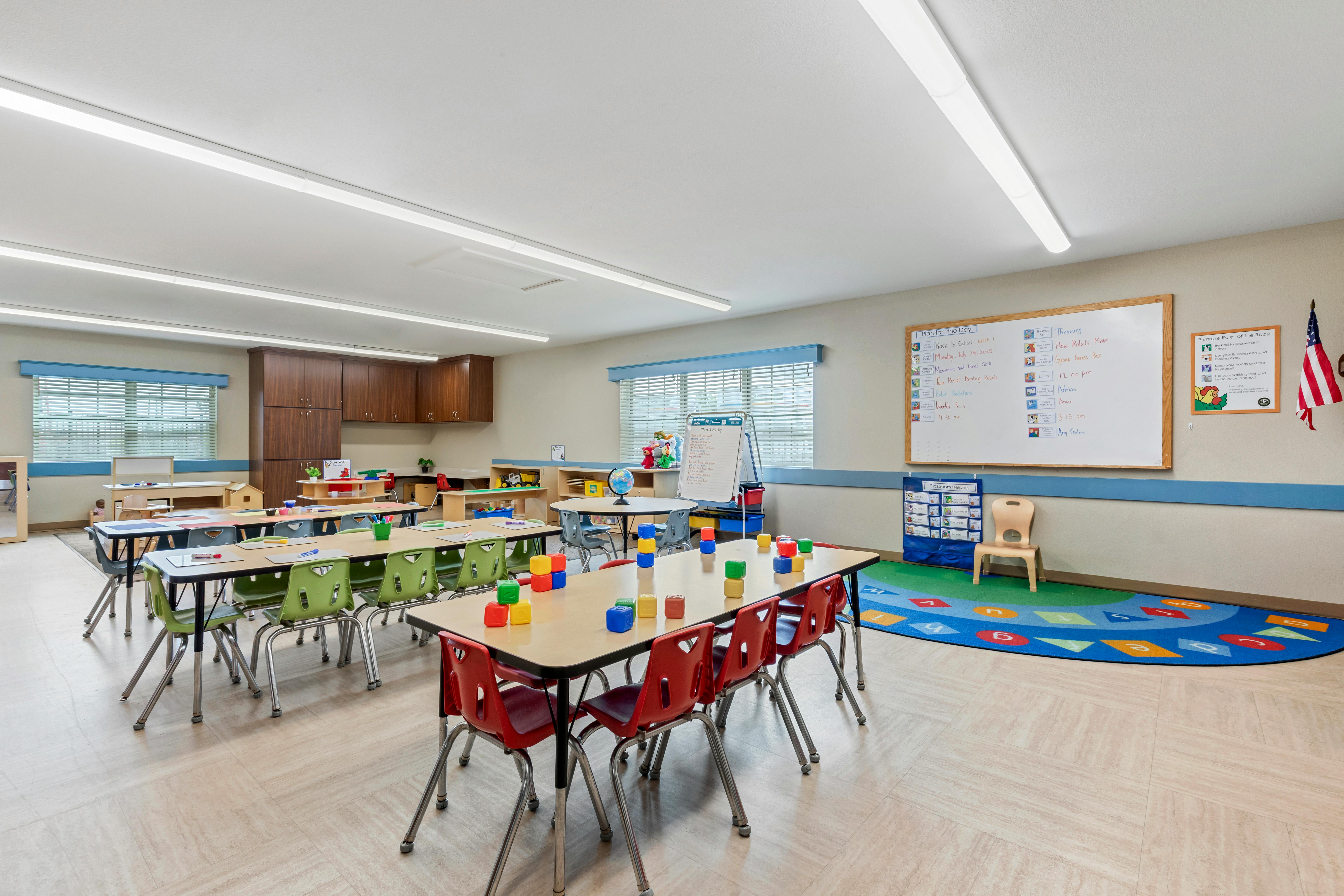 Classroom with child-sized tables and chairs, a whiteboard, and a colorful rug
