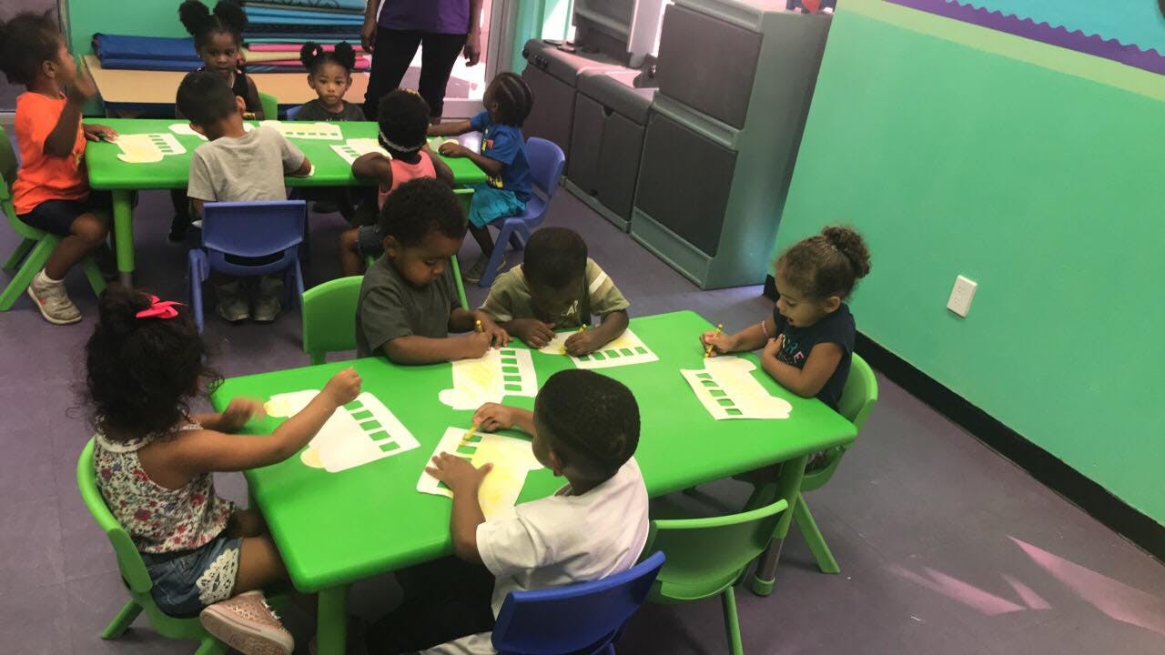 Children sitting at green tables in a classroom