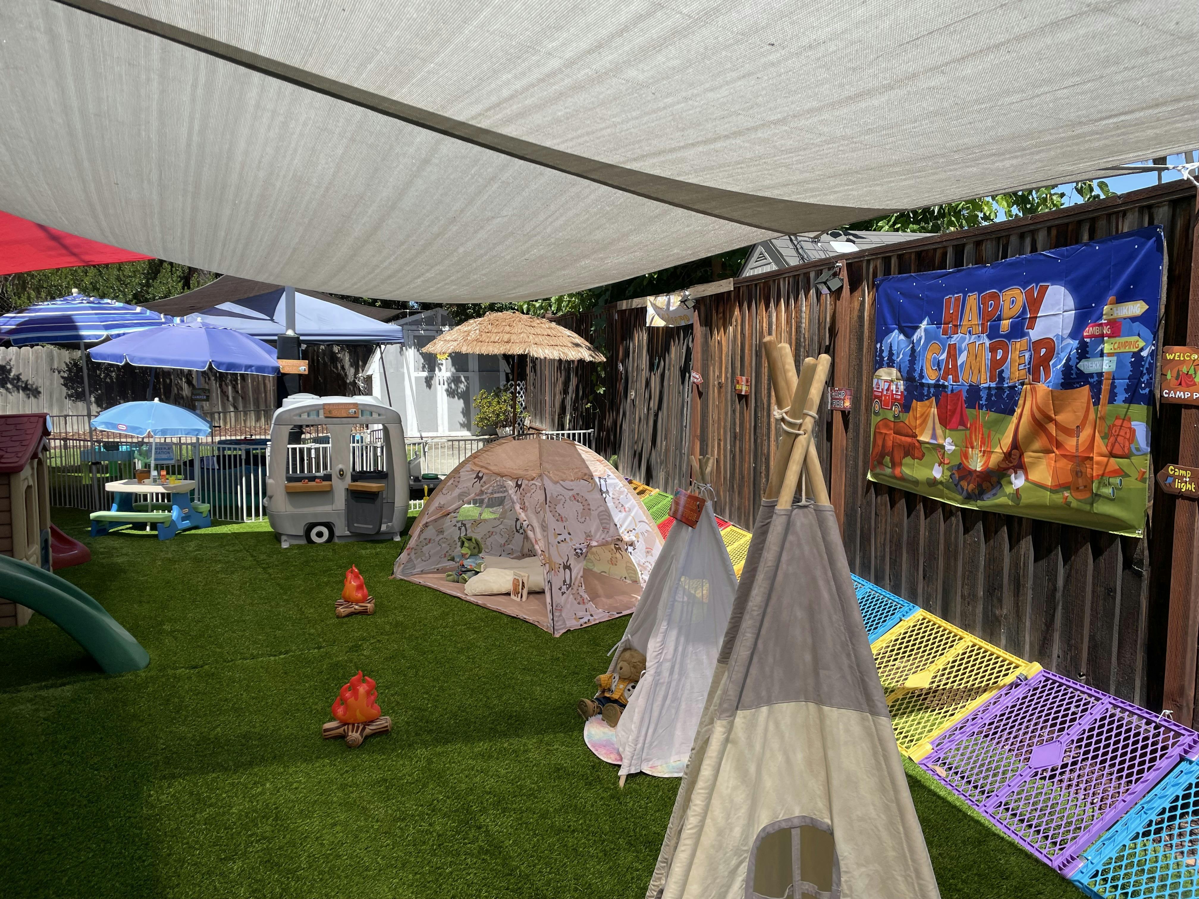 Play area for children with tents and a Happy Camper banner on artificial grass