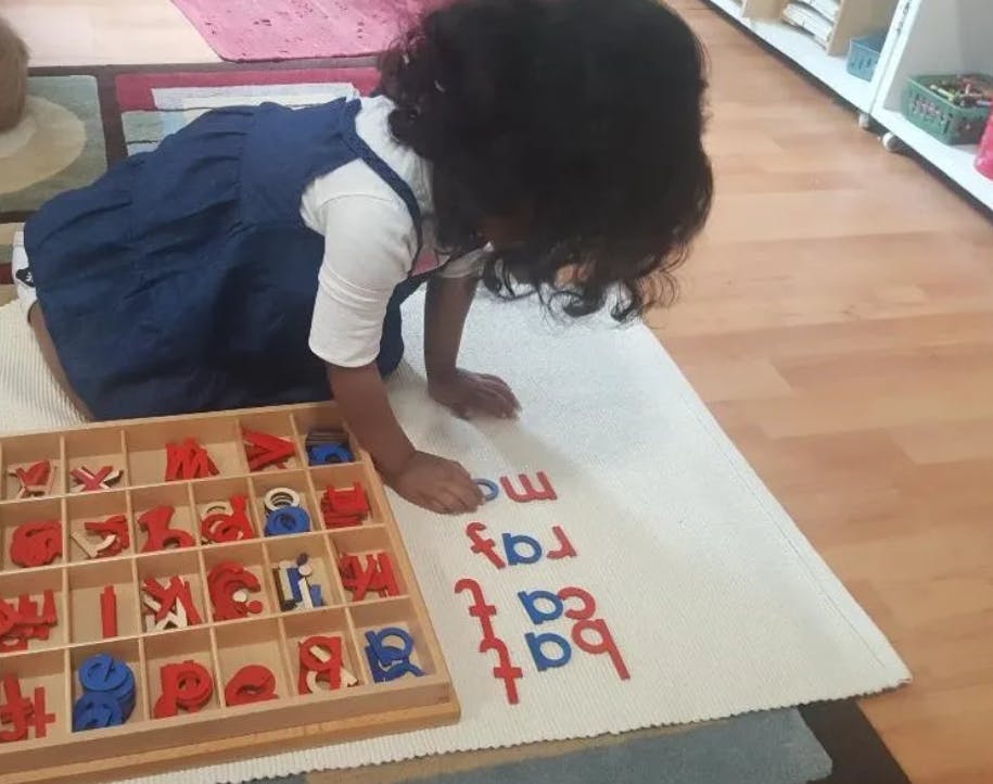Child on knees arranging letter tiles on a mat