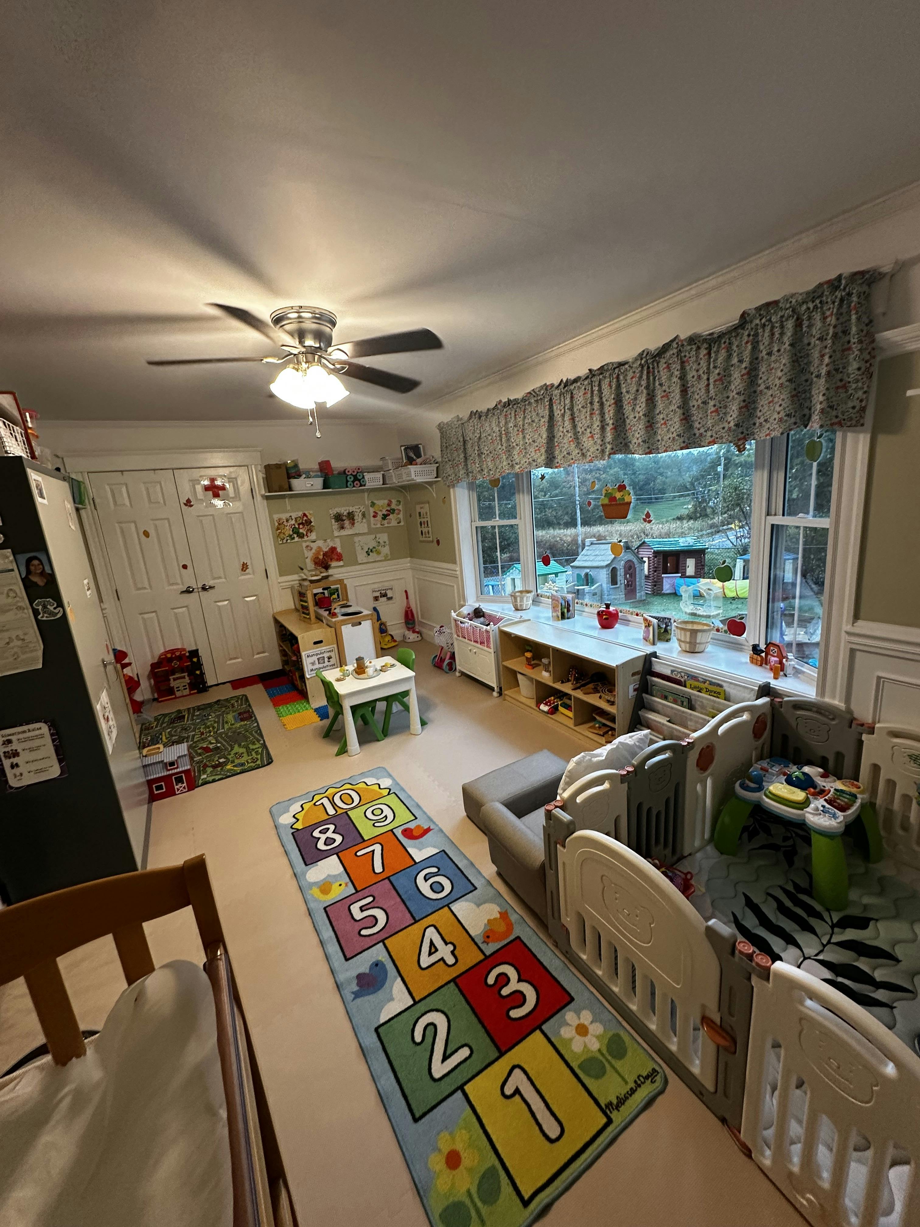 Playroom with a hopscotch rug, cribs, and a window overlooking a yard