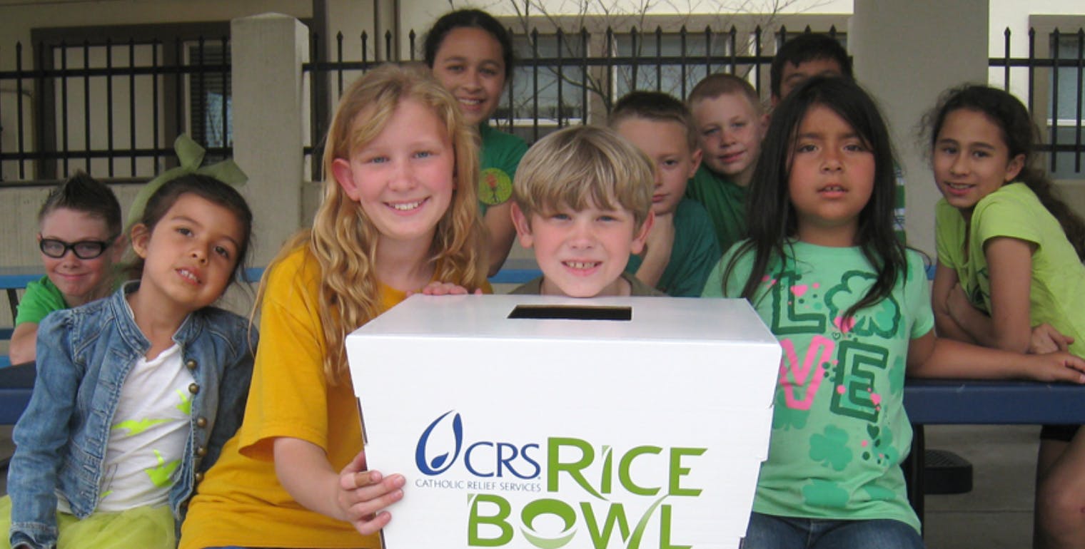 Children holding a white box with "CRS Rice Bowl" logo