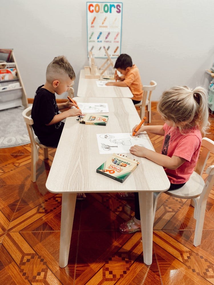 Three children coloring at tables in a classroom