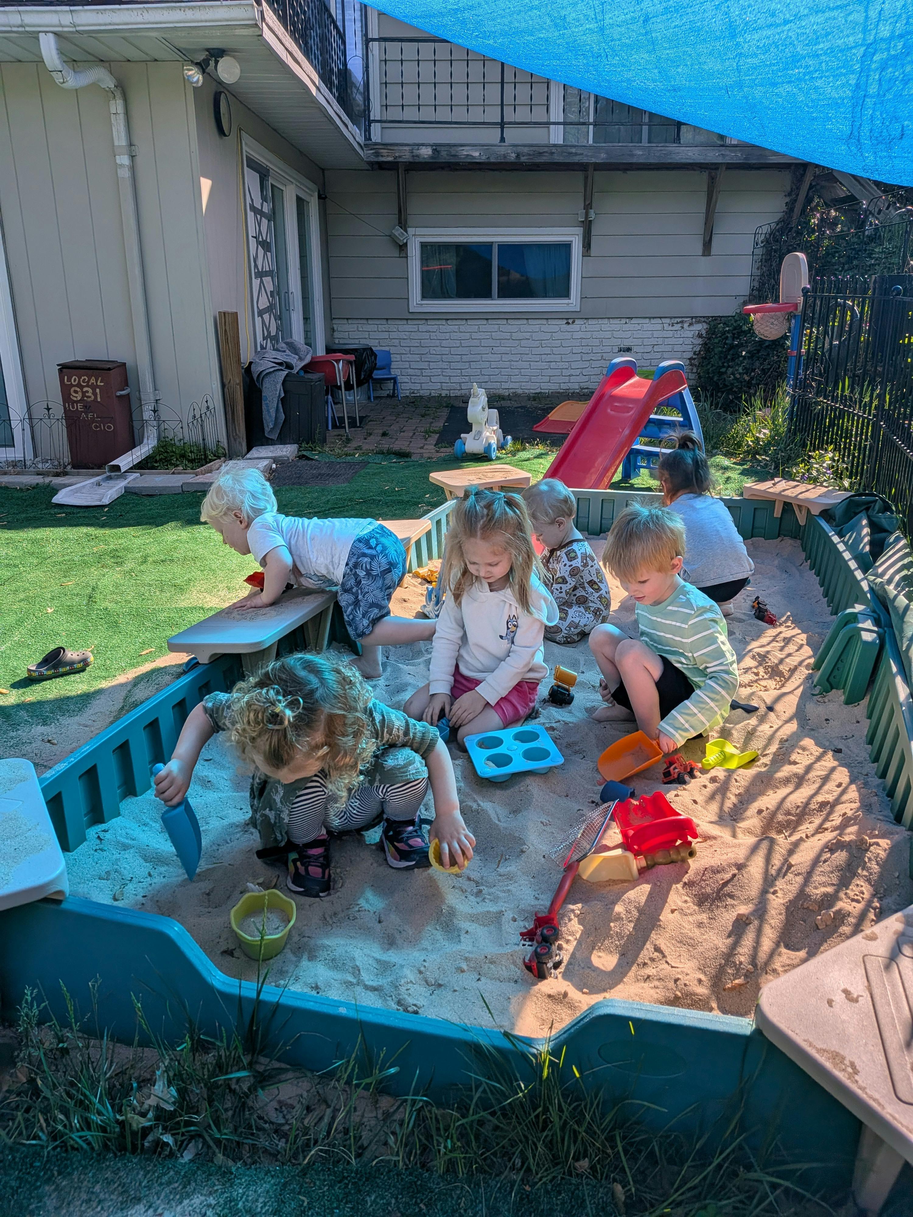 Group of children playing with toys in a backyard sandbox