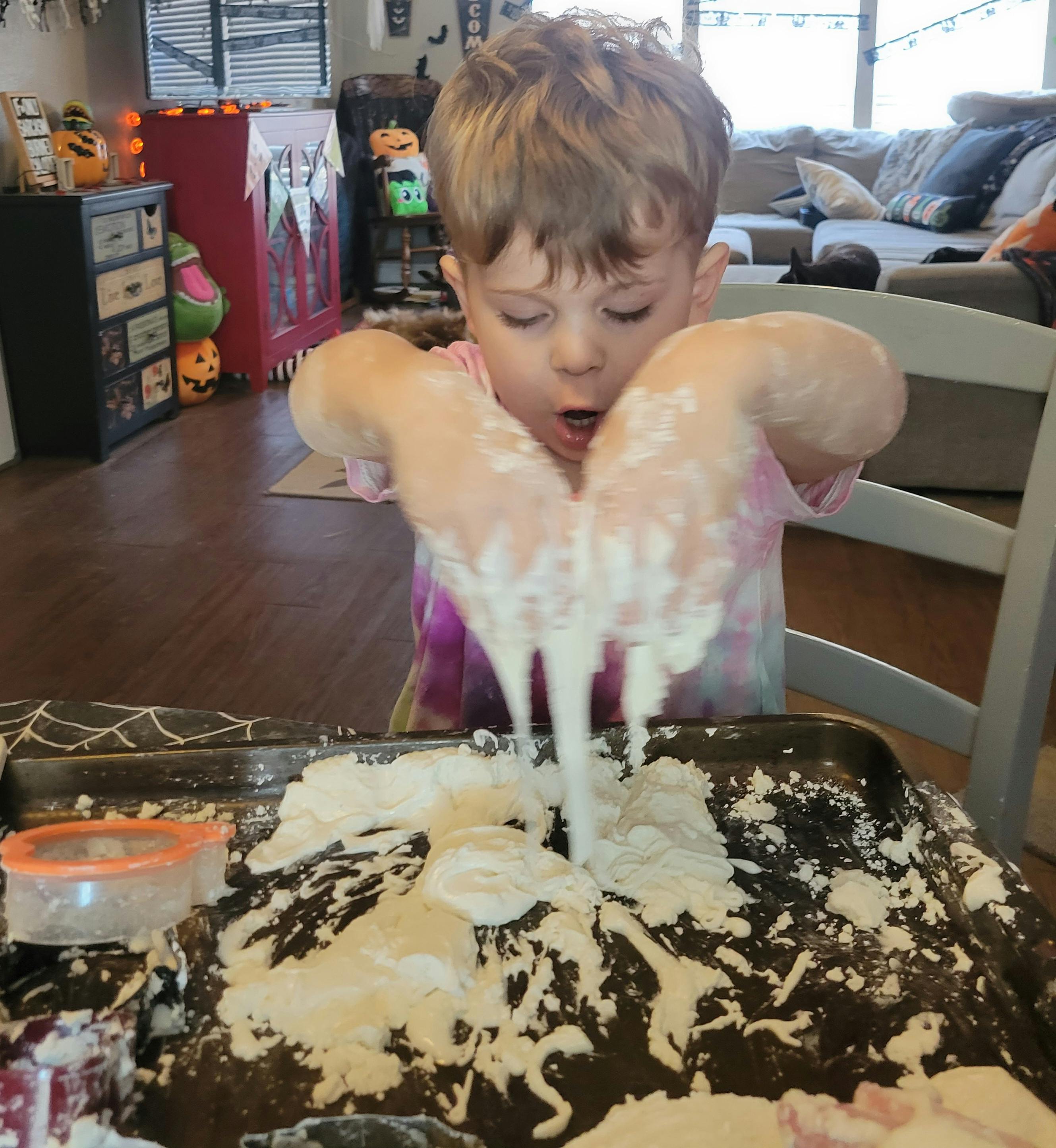 Child playing with white dough or slime in a tray