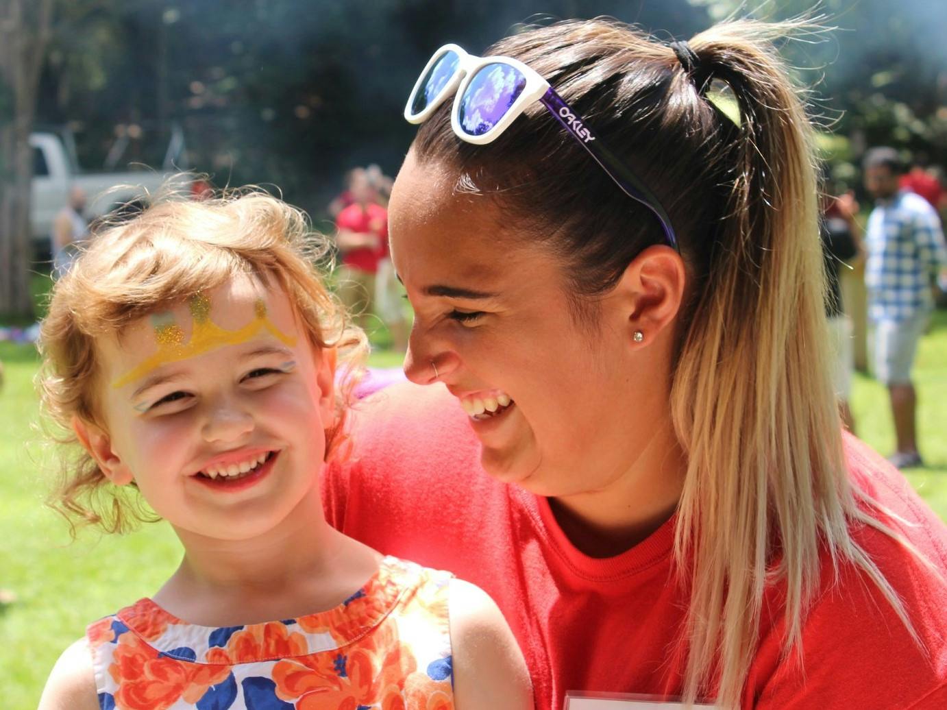 Person with sunglasses on head looking at child with face paint