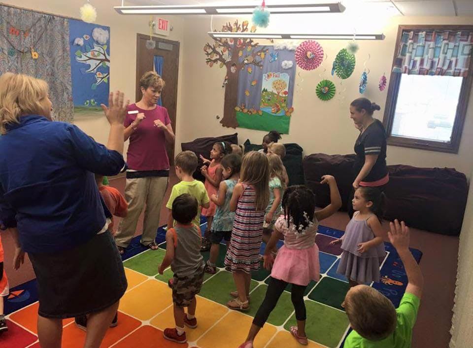 Adults and children dancing on a colorful mat in a room
