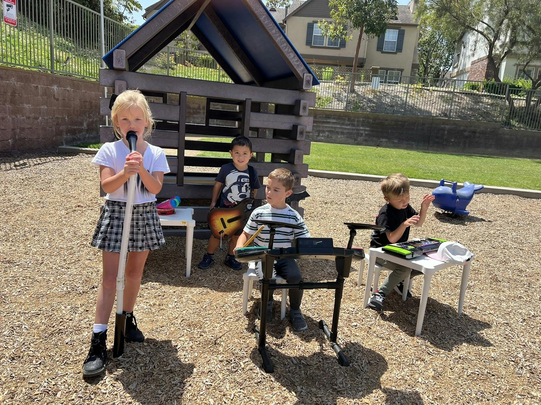 Four children performing music with toy instruments on a playground