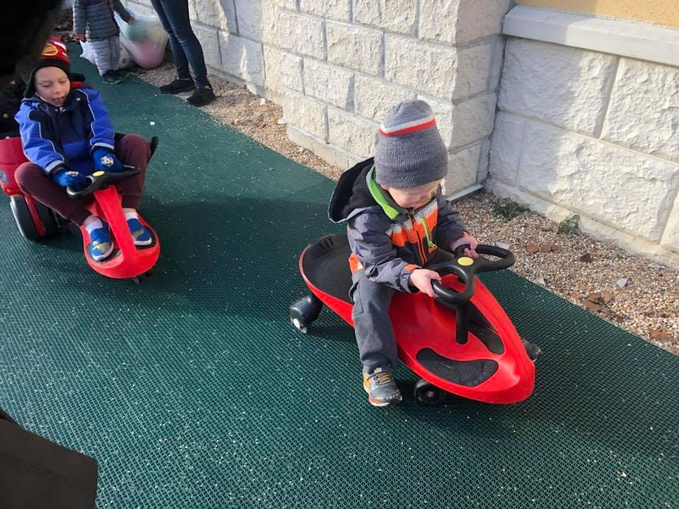 Two children riding red toy vehicles outdoors