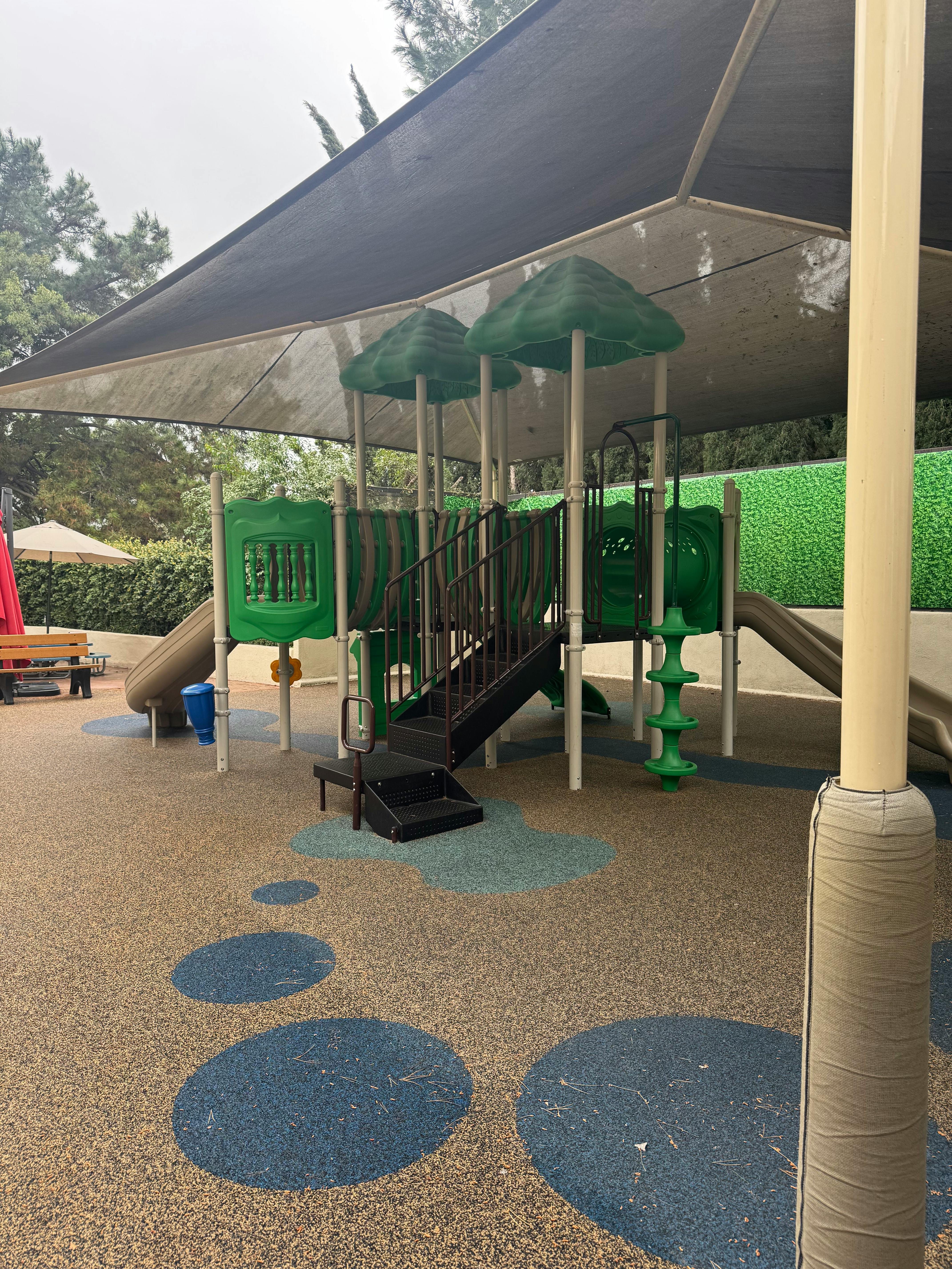 Playground with green and black equipment under a large shade canopy