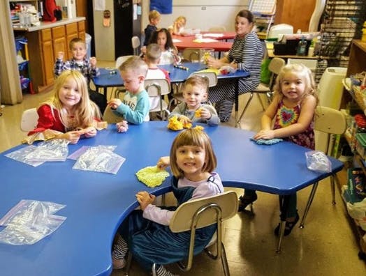Children and adults sitting at tables in a classroom