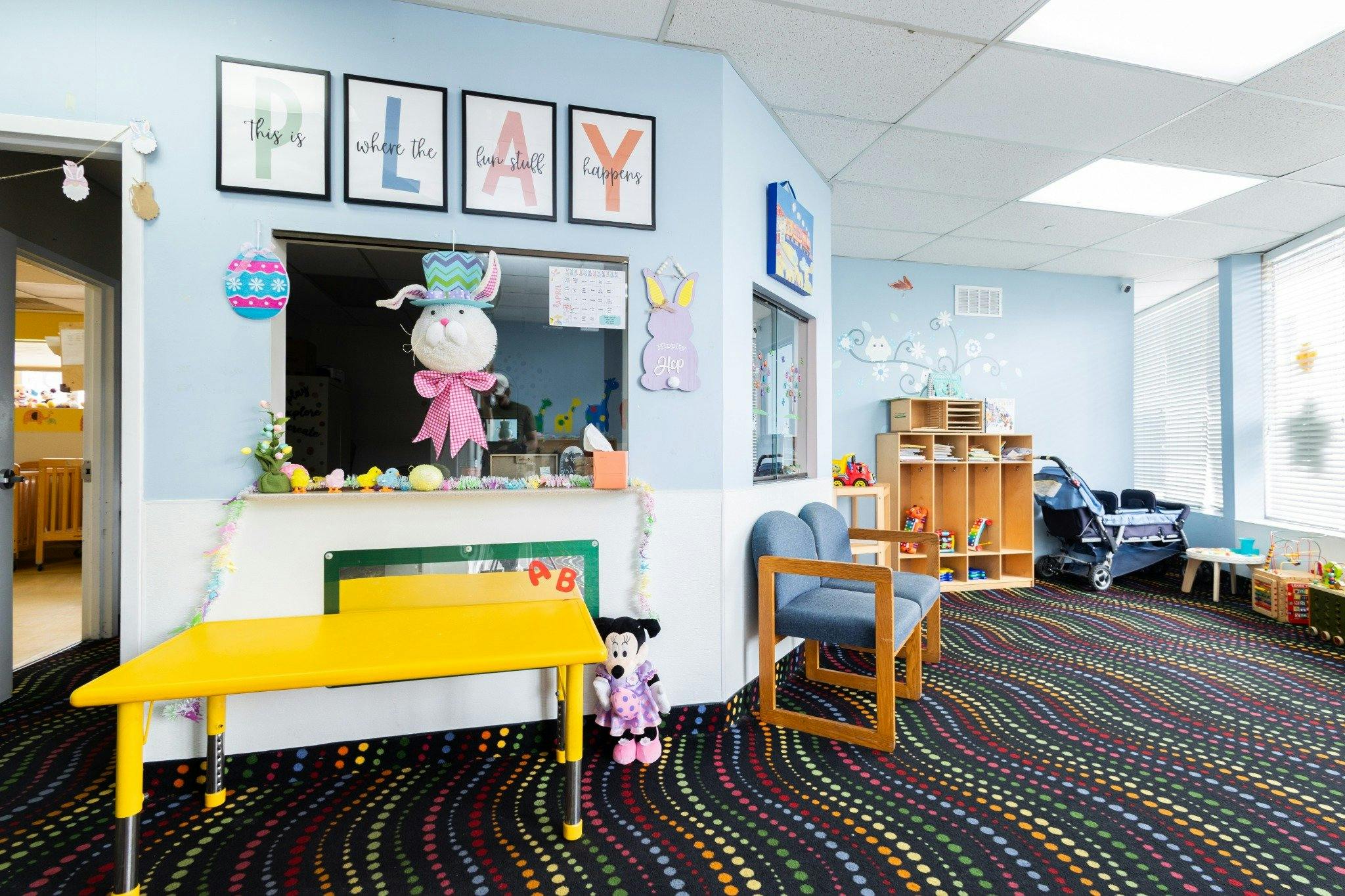 Childcare playroom with a yellow table, chairs, shelving, and Easter decor