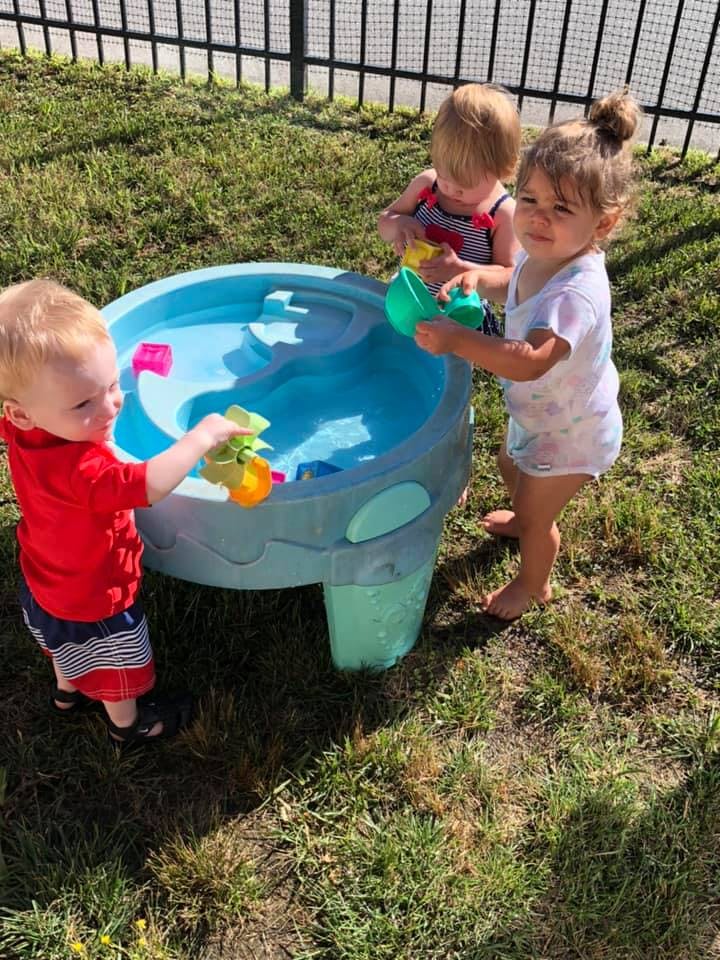 Three children playing with a water table outdoors