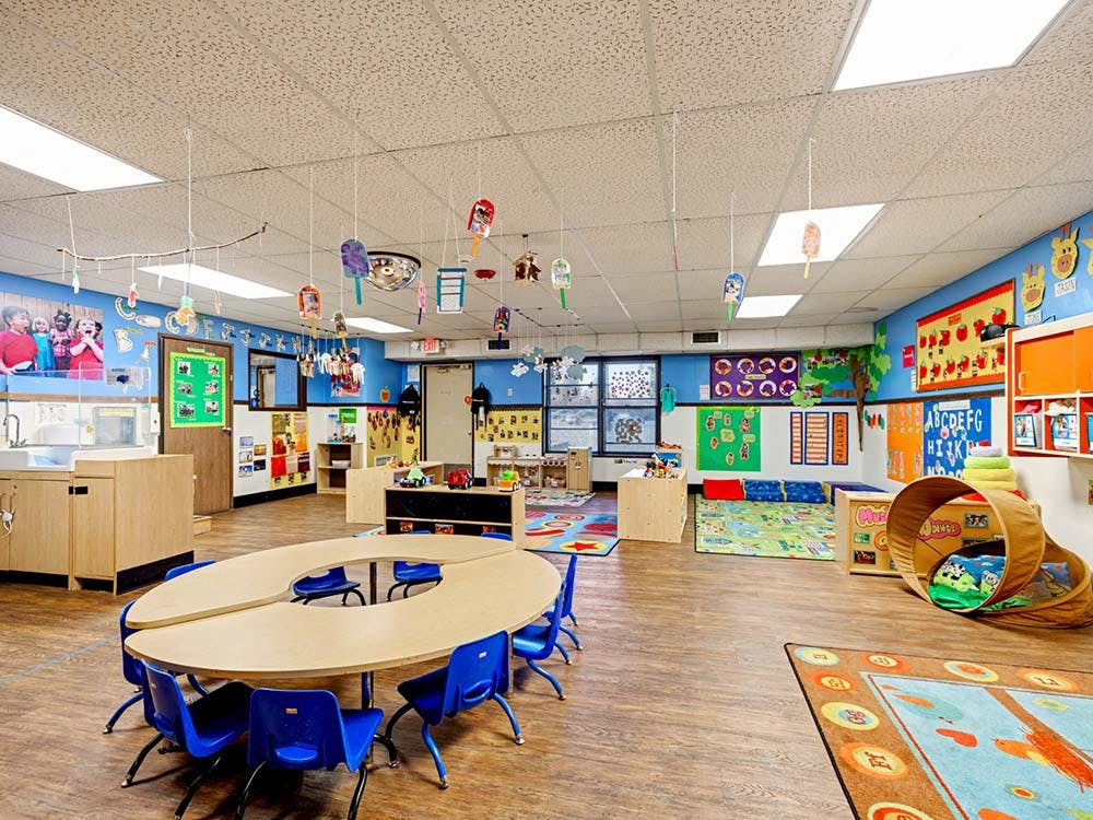 Classroom with child-sized tables and chairs, artwork on walls, and various play areas
