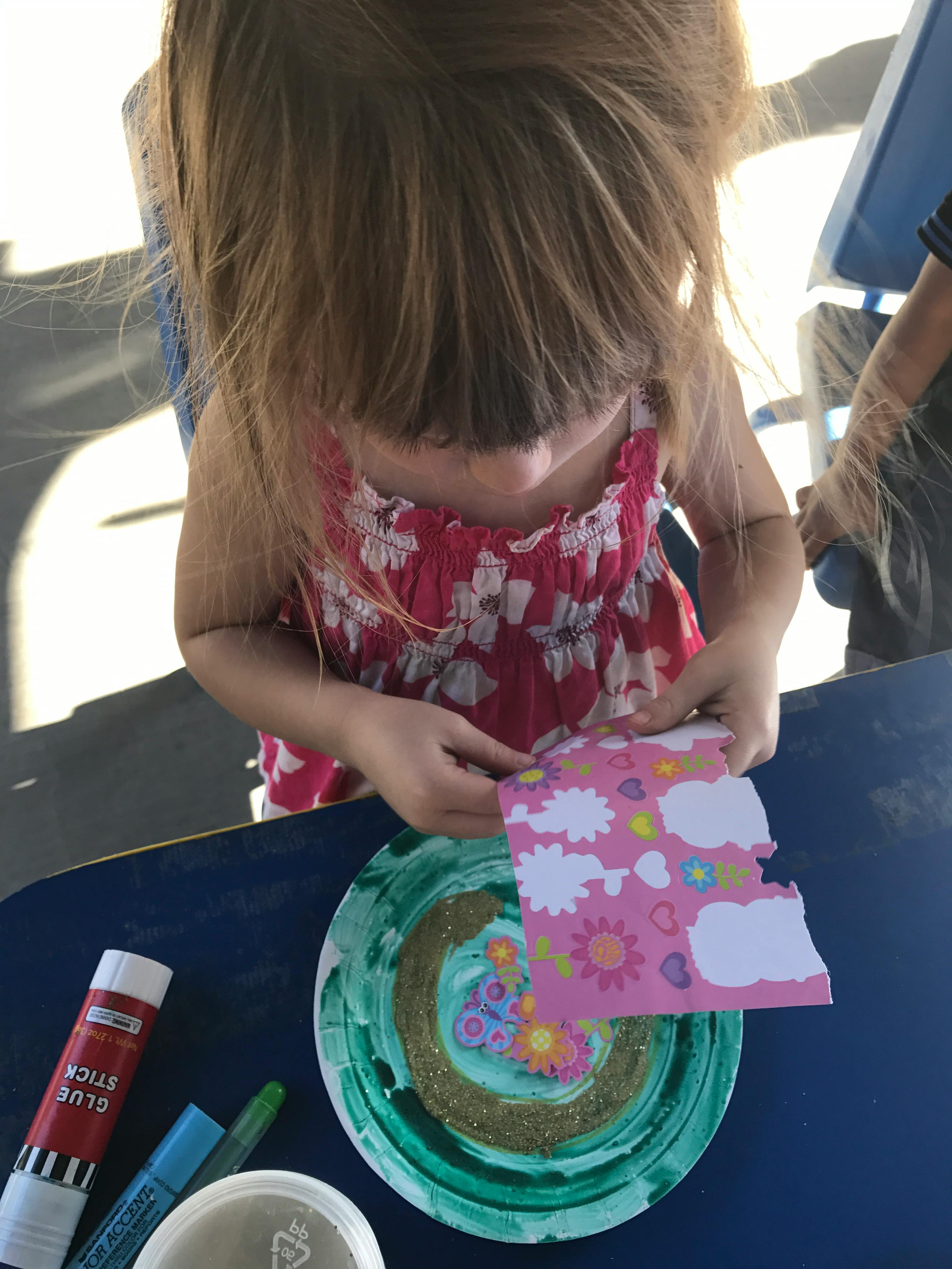 Child holding a piece of patterned paper over a decorated paper plate