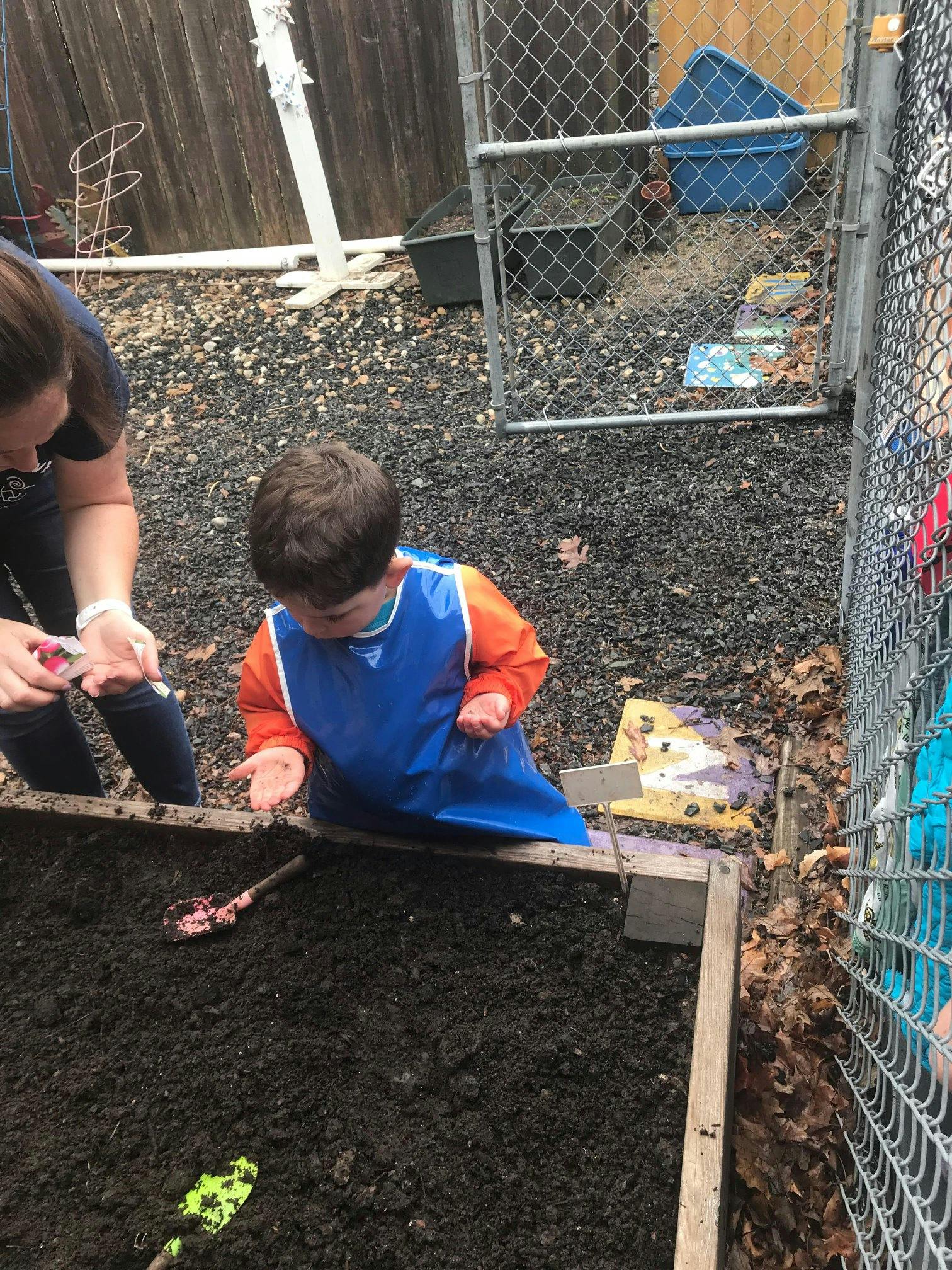 Person and child in a blue smock planting in a garden bed