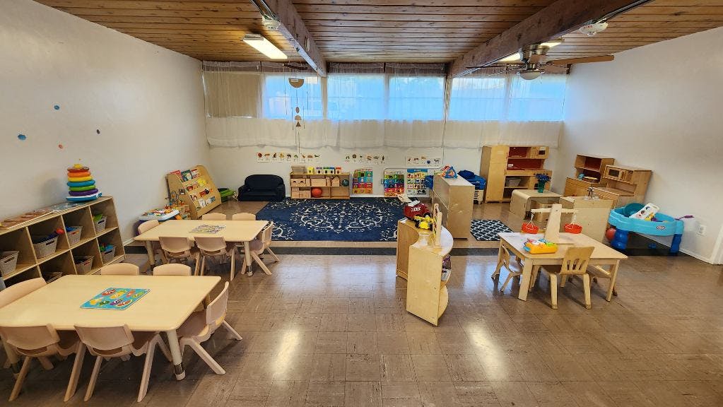 Classroom with small tables and chairs, shelves, and play areas
