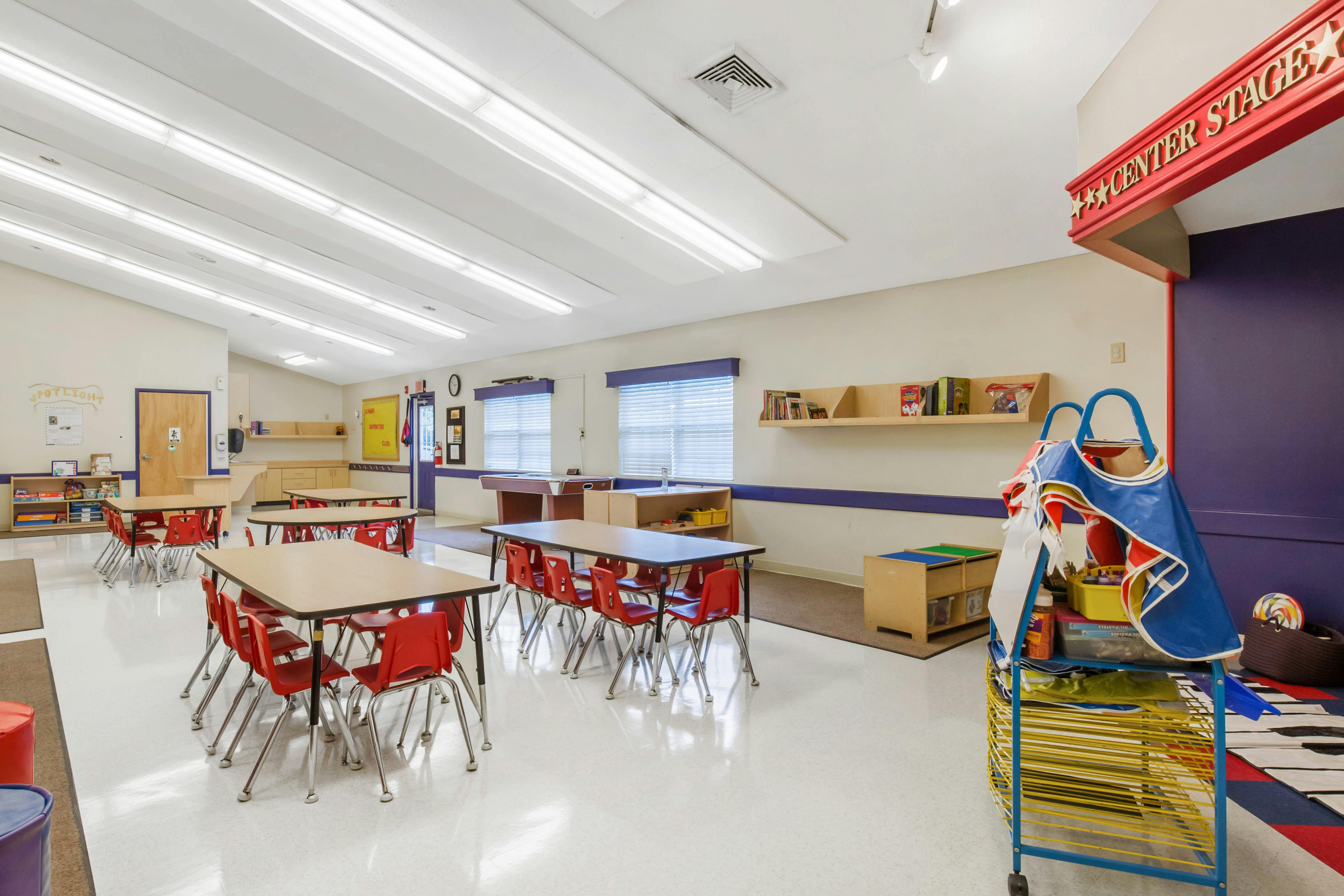 Classroom with empty tables and red chairs, a stage area labeled "CENTER STAGE"