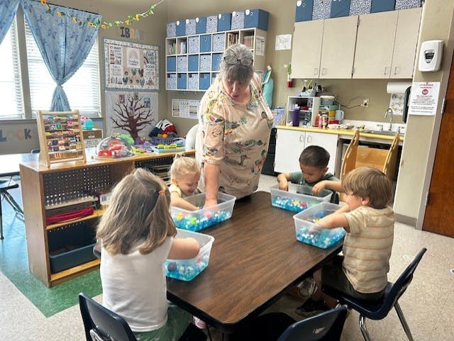Adult and children playing with toys in clear bins at a table