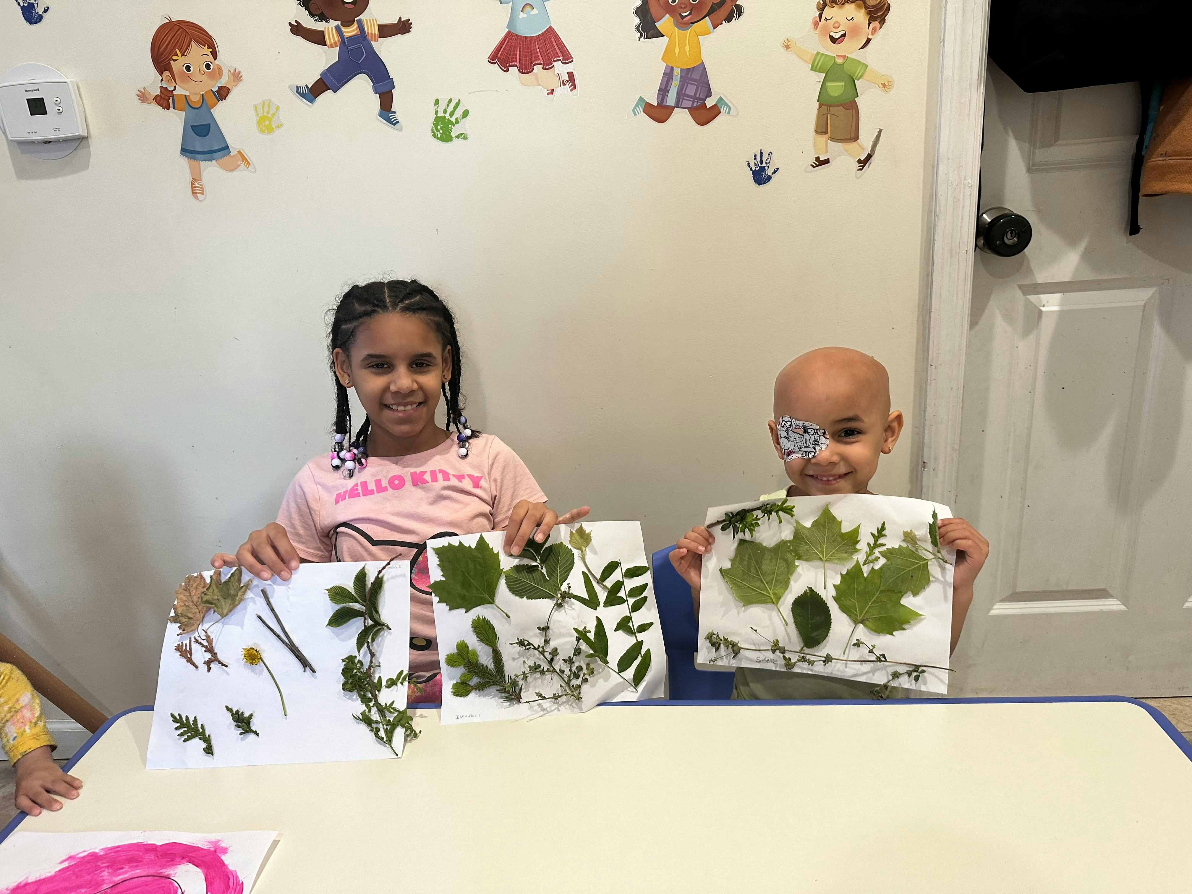 Two children holding up papers with pressed leaves and flowers