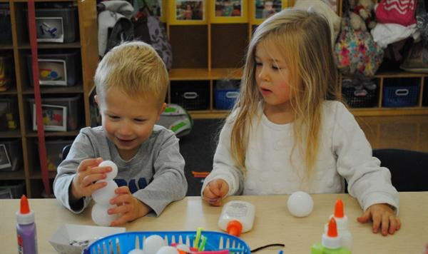 Two children at a table doing crafts with craft supplies