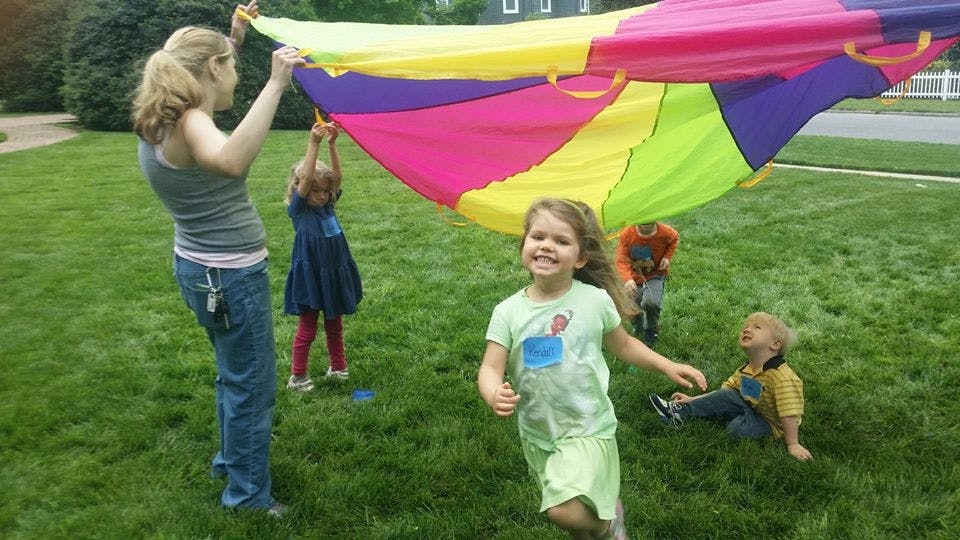 People and children playing with a colorful parachute on grass
