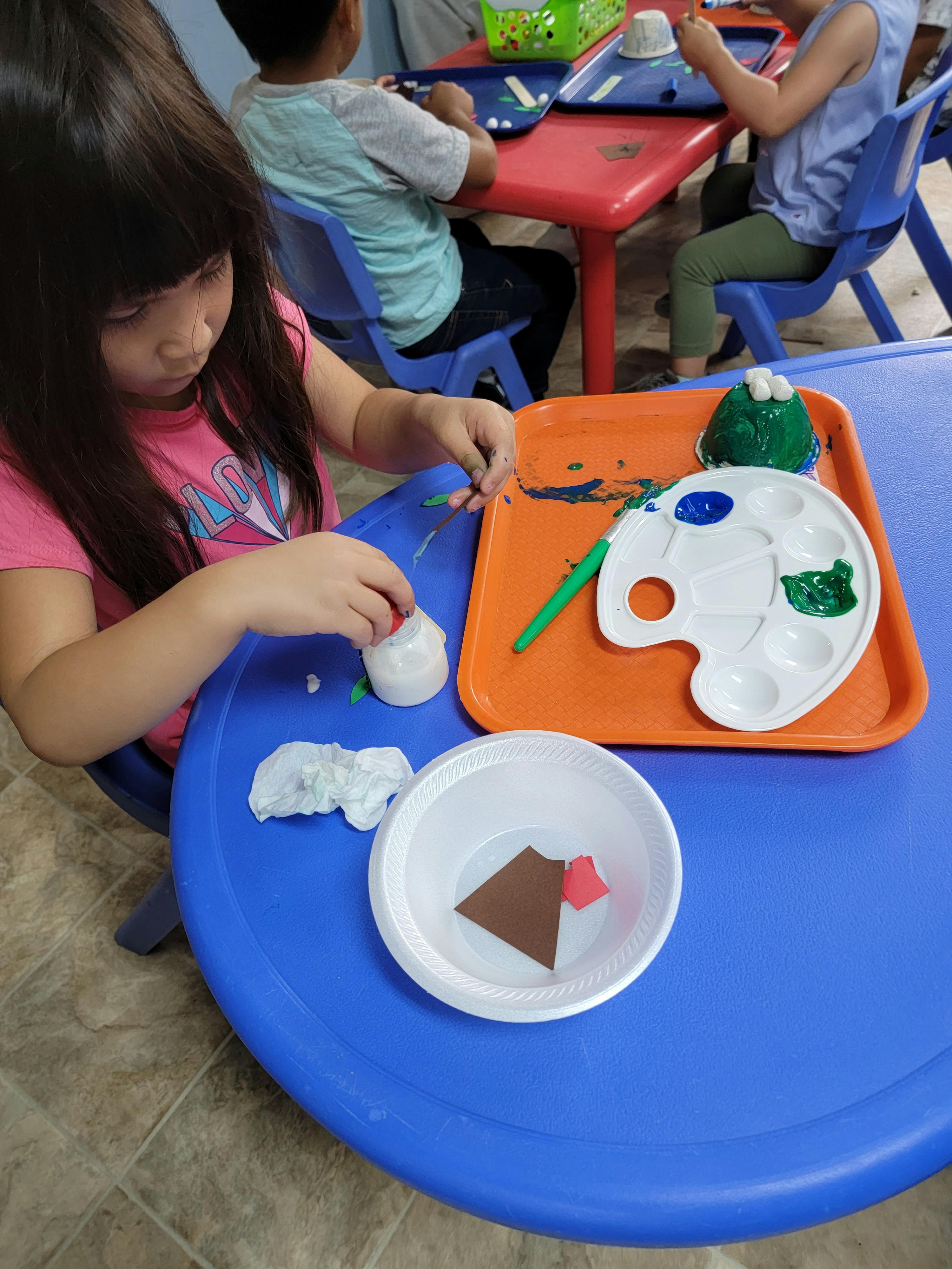 Child painting a craft project at a blue table