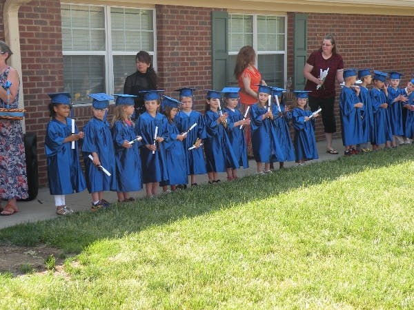 Children in blue graduation gowns and caps holding diplomas
