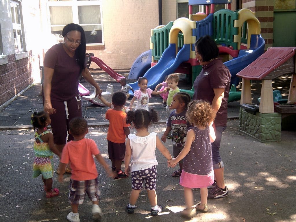 Two adults and multiple children holding hands in a circle on a playground