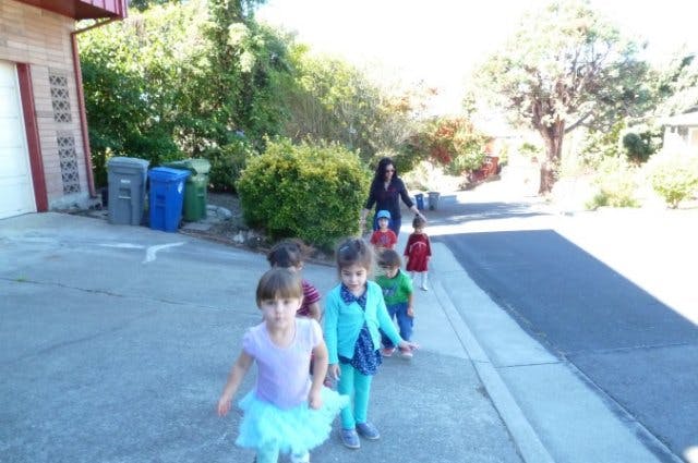 Person walking with a line of children on a sidewalk