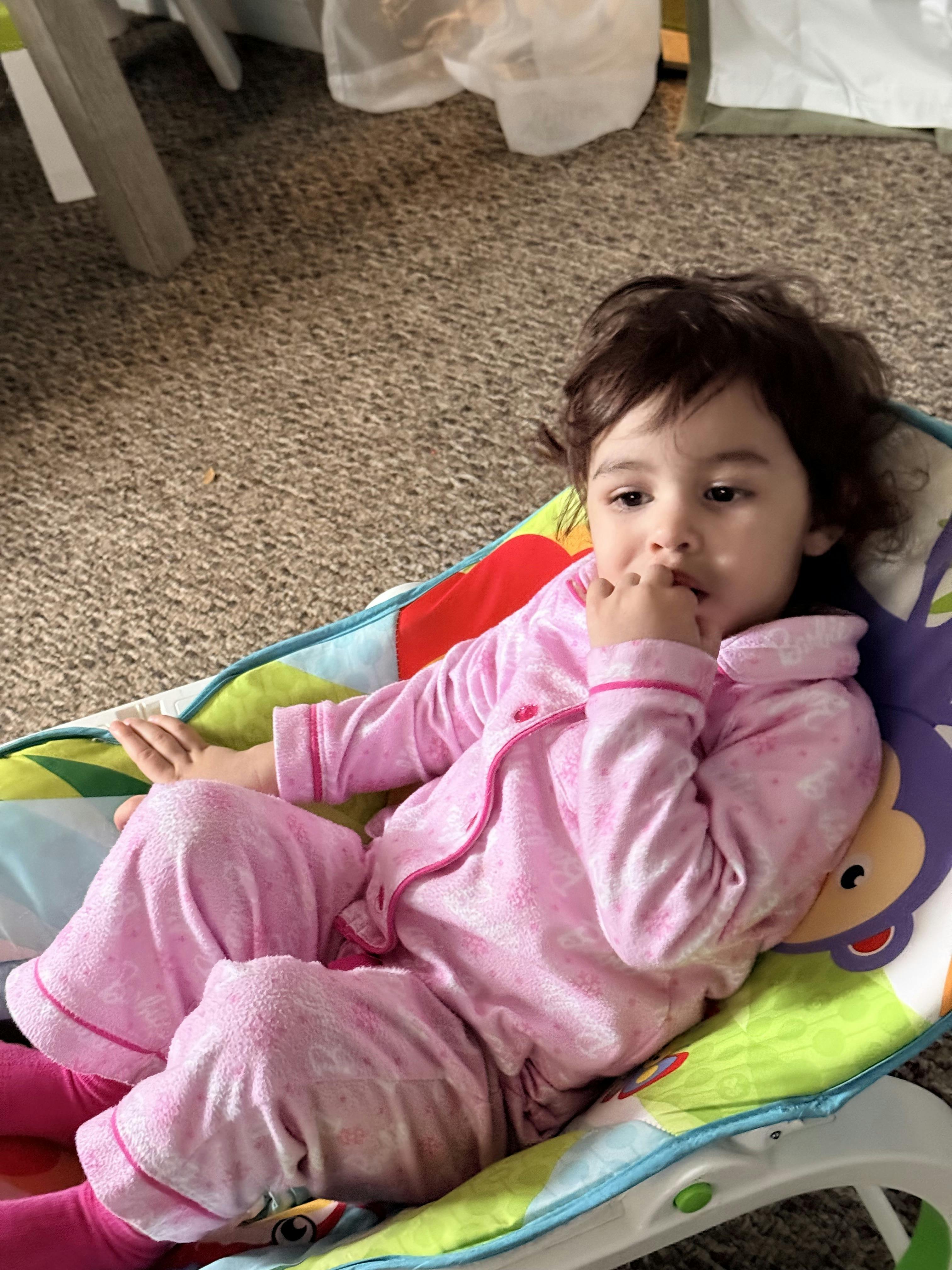 Child in pink pajamas lying in a patterned bouncer chair
