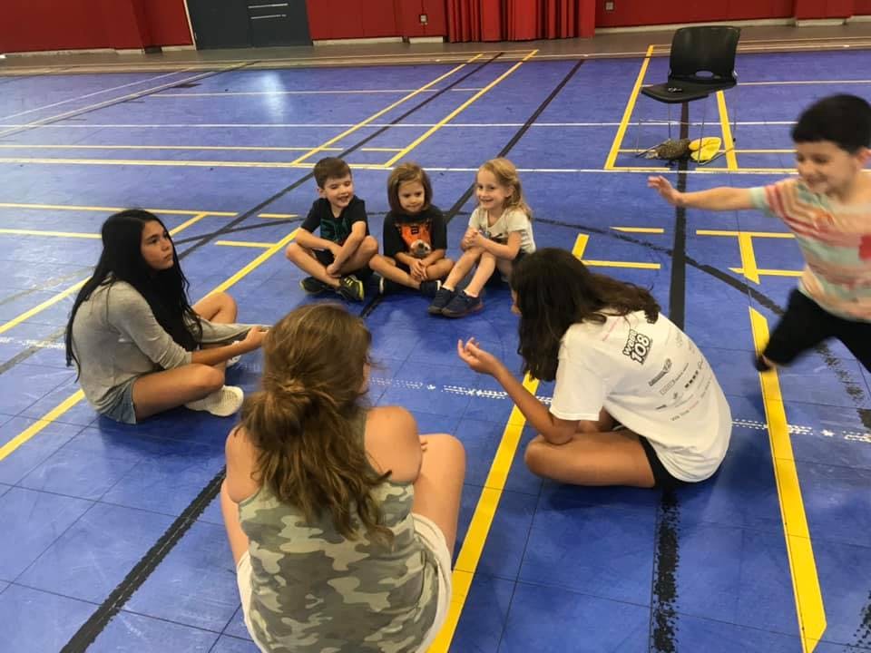 People and children sitting in a circle on a blue court